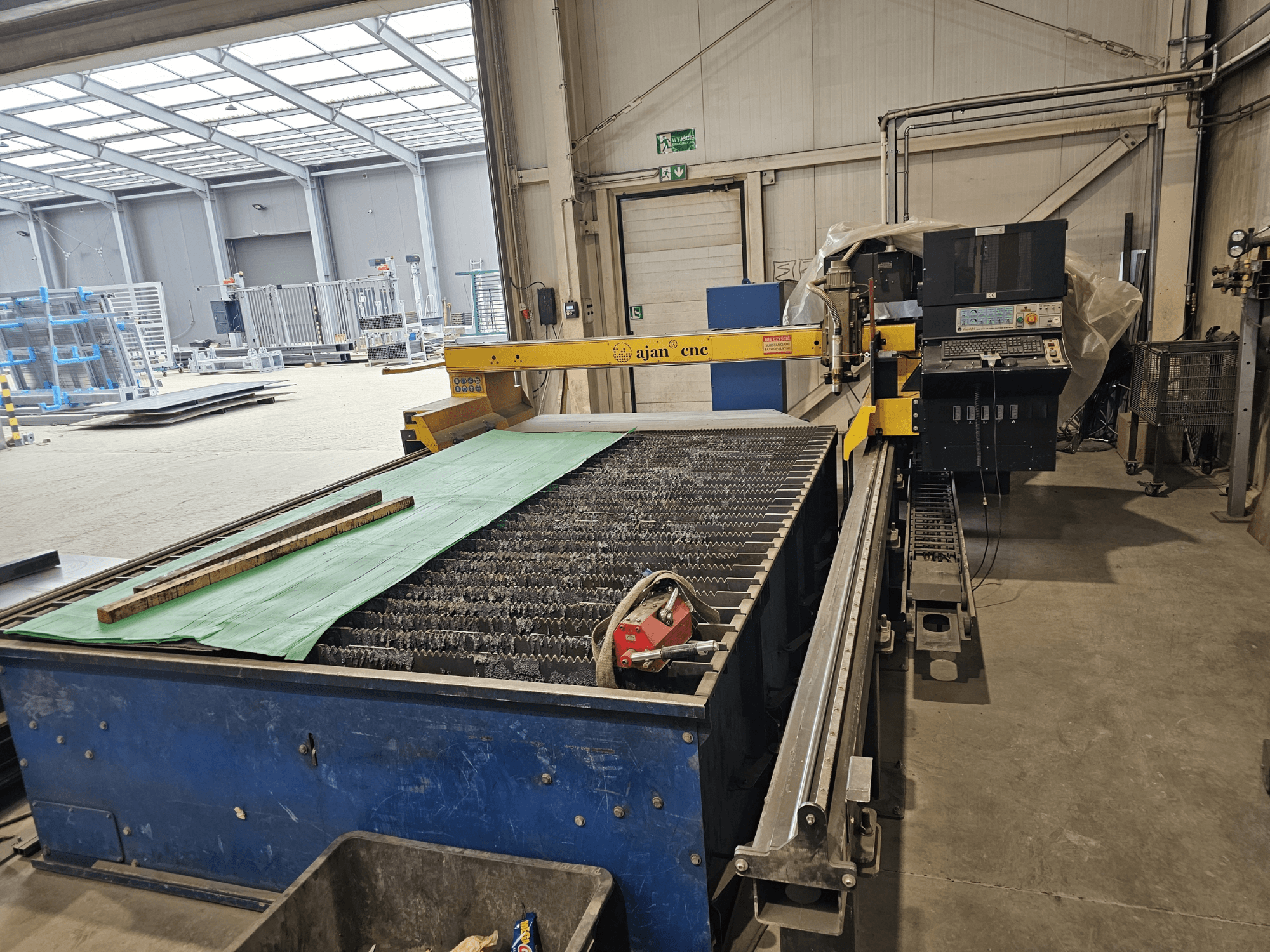 AJAN PP16011 Automaattinen plasmaleikkauskone sivukuvassa, jossa on leikkuupöytä ja ohjauspaneeli työpajaympäristössä.