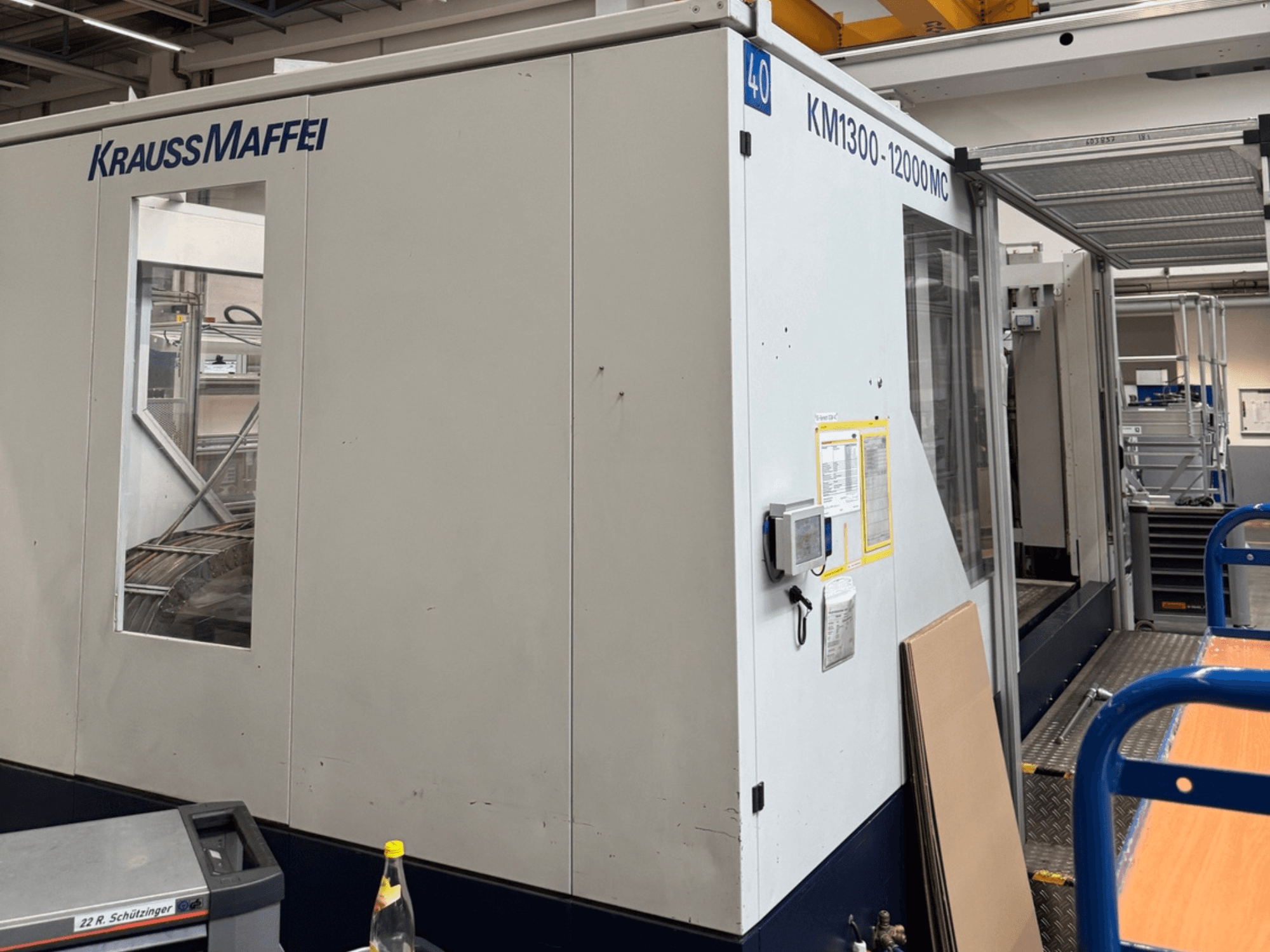 Krauss Maffei Hydraulinen ruiskuvalukone KM1300-12000 MC, sivukuva, jossa näkyy ohjauspaneeli ja toimintatila.