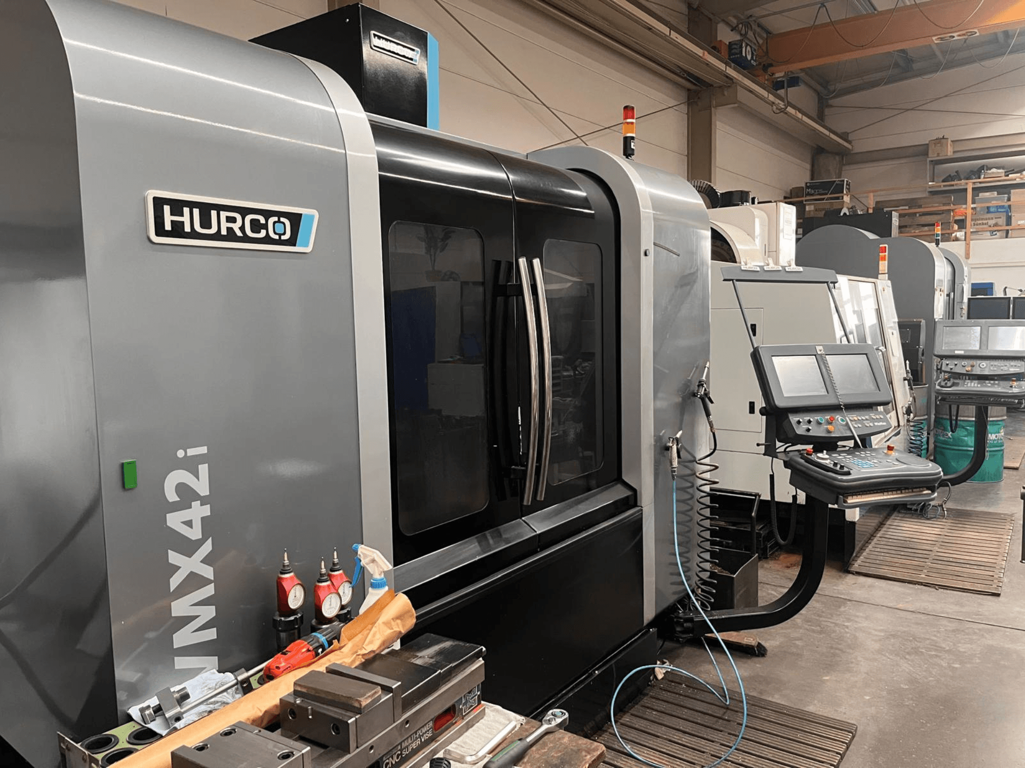 Hurco VMX42i CNC-kone työpajassa, etukuva, jossa ohjauspaneeli ja erilaisia työkaluja työpöydällä.