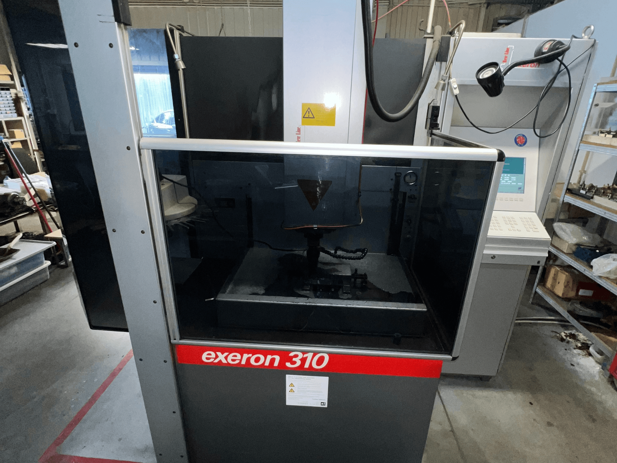 Exeron 310 -koneen etunäkymä, jossa näkyy lasikammio ja ohjauspaneeli sekä työpisteen hyllyt.