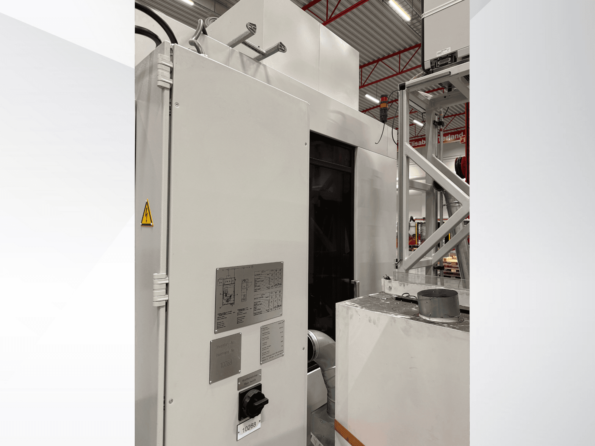 Sivukuva valkoisesta teollisuuskoneesta, jossa on ohjauspaneeli ja varoituskyltti, osa automaattista järjestelmää.