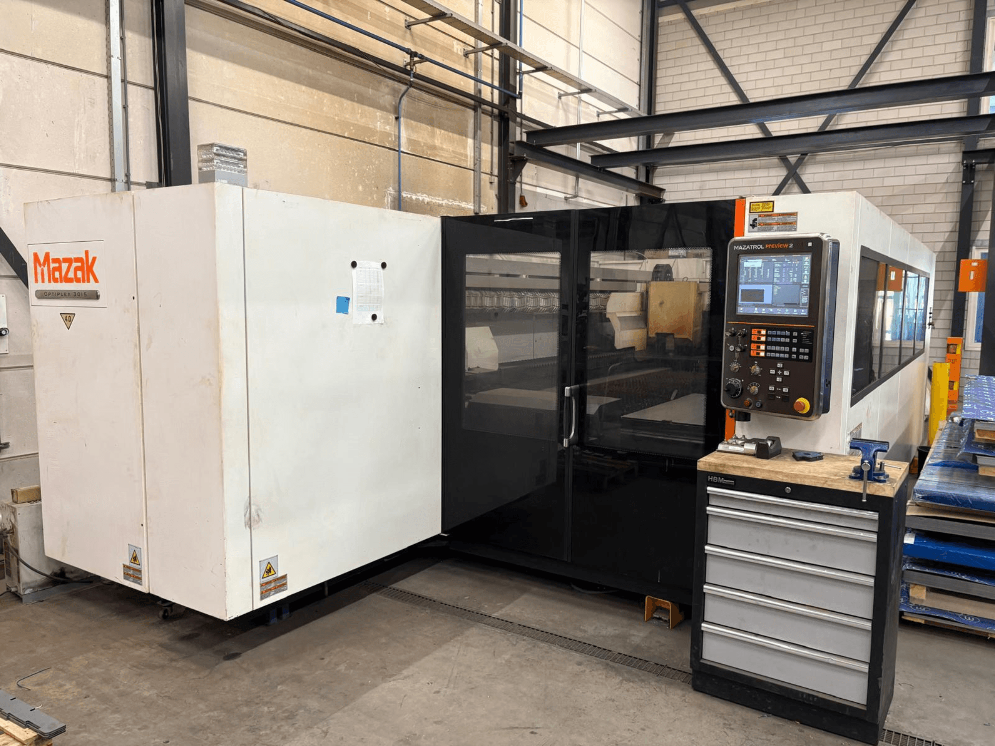 Mazak Optiplex 3015 CO2-laserleikkauskone, etunäkymä, jossa näkyy ohjauspaneeli ja teollisuusympäristö.