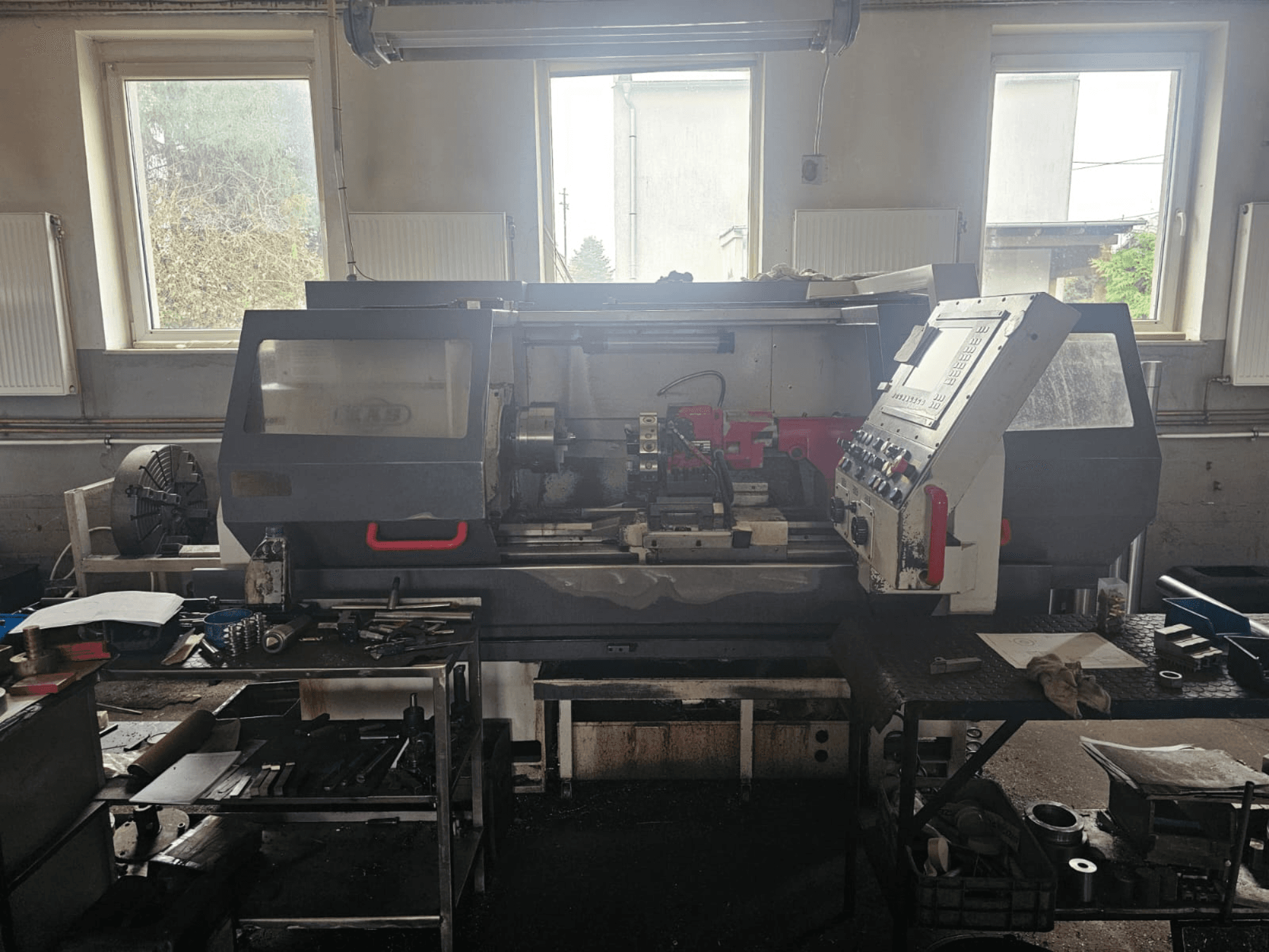 Sorvinkone työpajassa, etukuva, ohjauspaneeli ja työkaluja pöydillä, ikkunoiden ympäröimänä ja sekainen työtila.