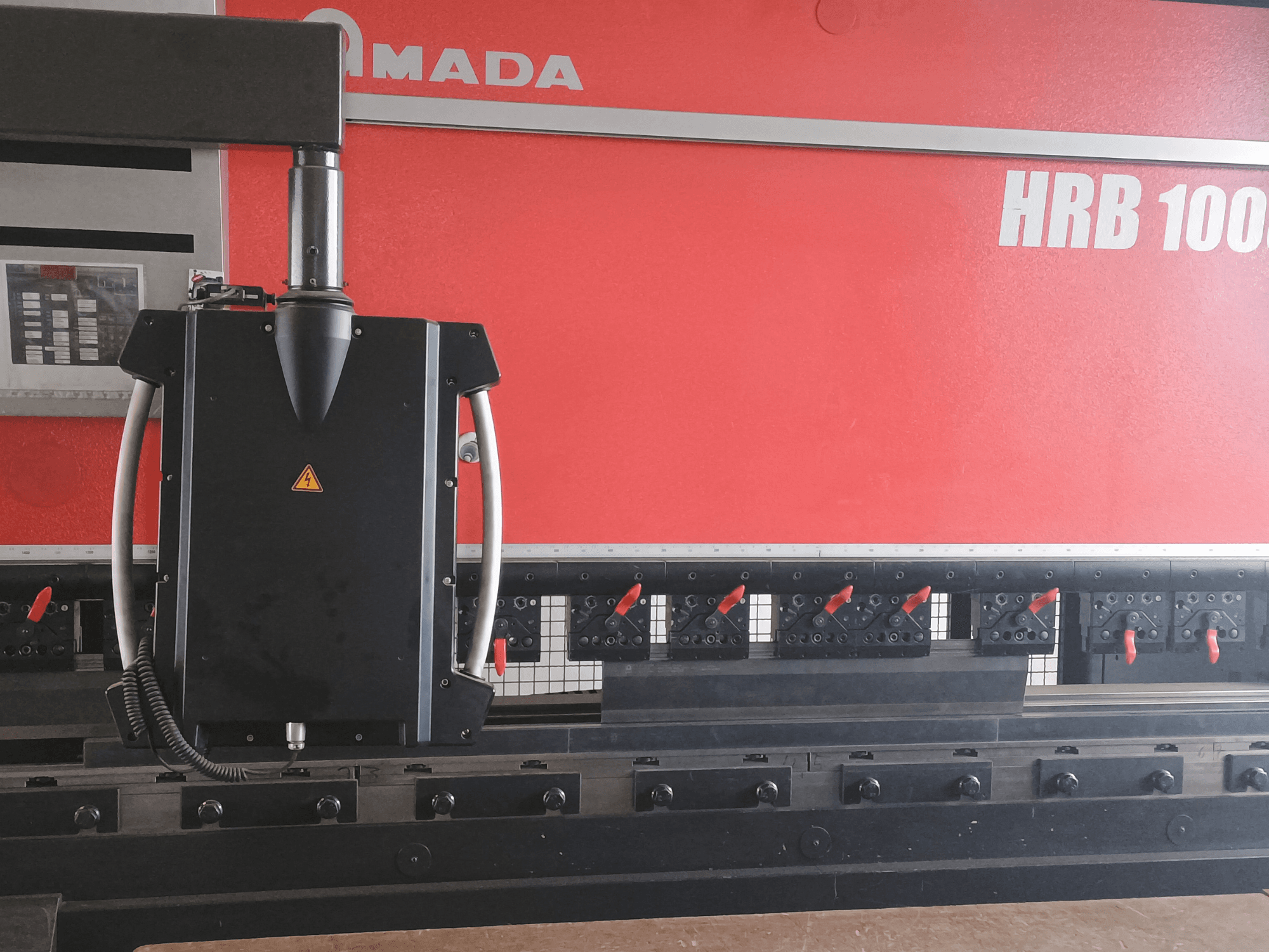 Amada HRB 100 -taivutuskoneen etukuva; mustassa ohjauspäässä on kartiosuutin ja säädettävät puristimet.