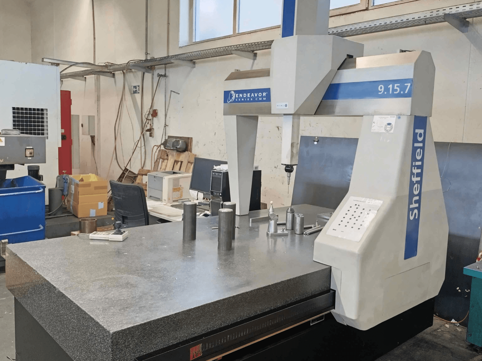 Koordinaattimittauskone Sheffield Endeavor 9.15.7 työpajassa, jossa on graniittipöytä ja metallisia työkappaleita.