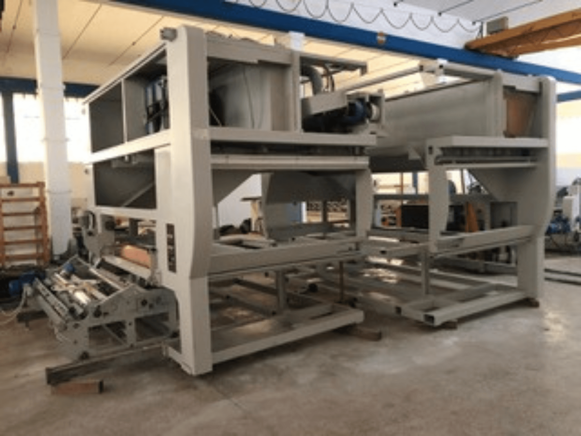 Teollisuuskone, jossa on useita kuljetinrullia ja suuri rakenne; sivukuva, harmaa väri, sijaitsee hyvin valaistussa tehtaassa.