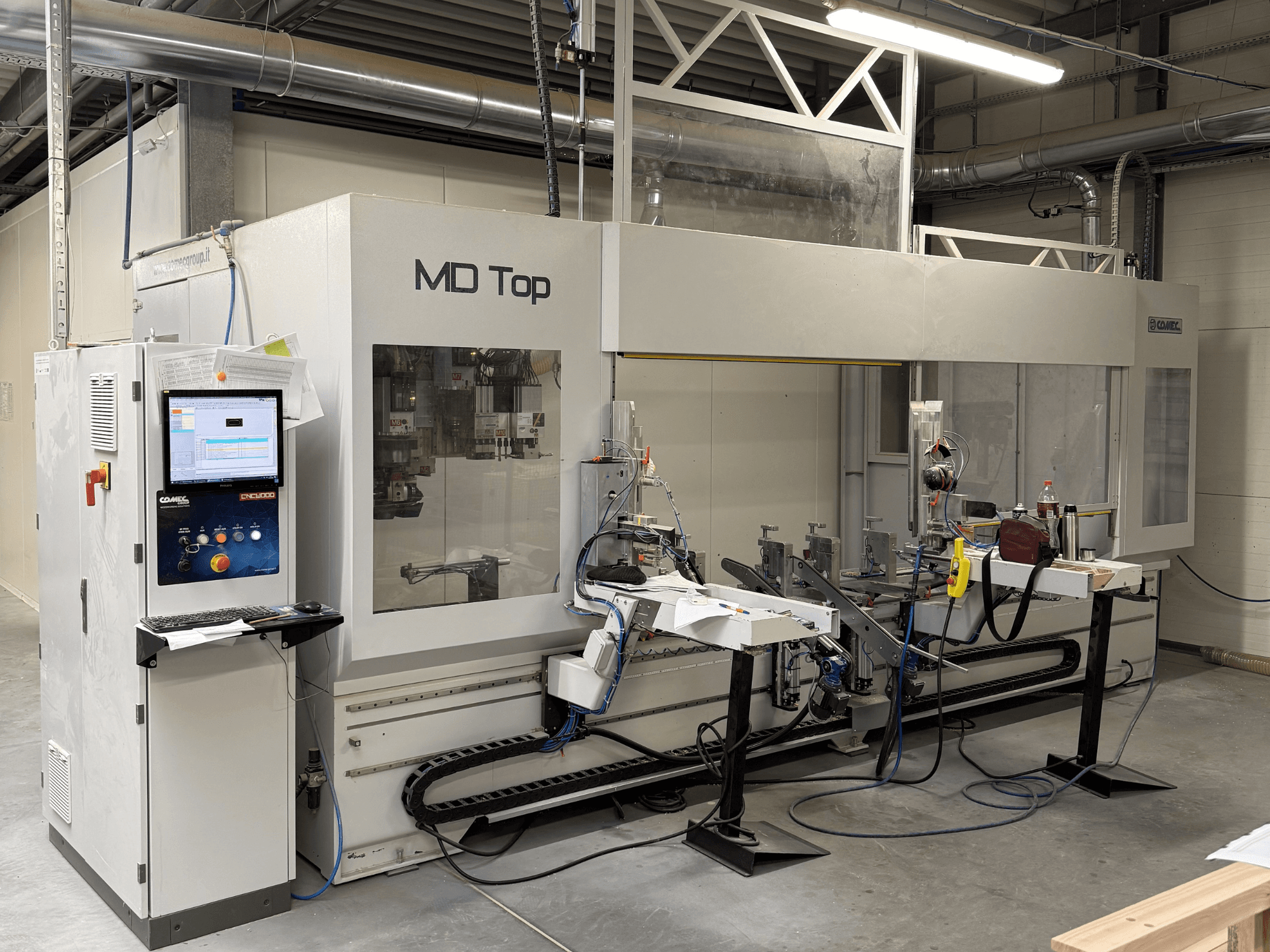 MD Top CNC-kone edestä katsottuna, jossa on ohjauspaneeli, robottivarret sekä työtila työkaluineen ja materiaaleineen.