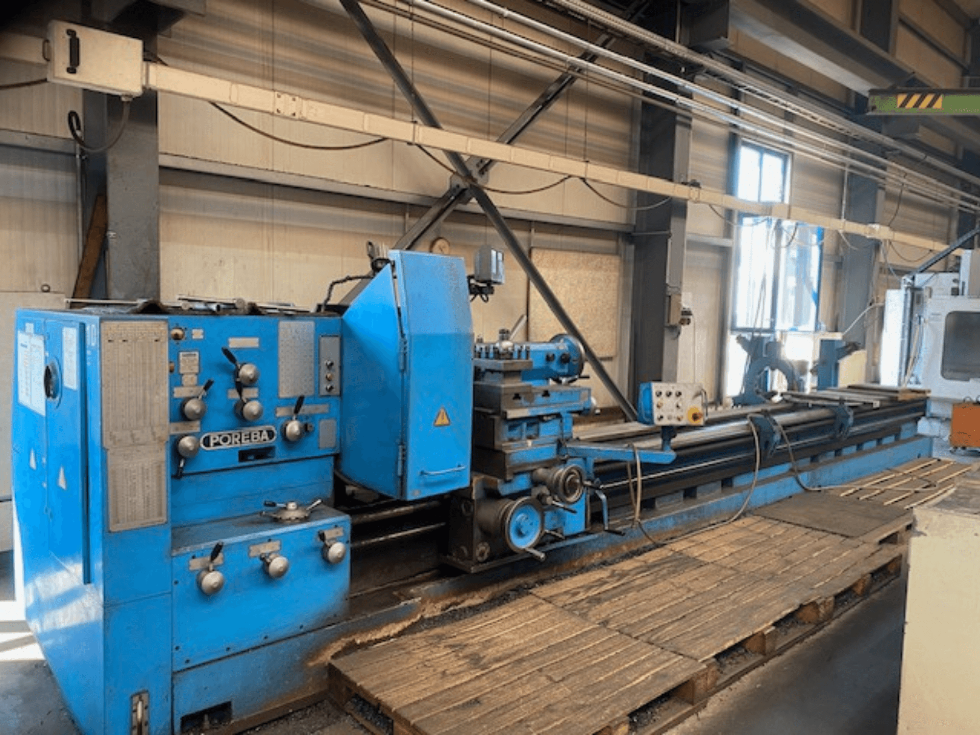 Sinisen POREBA-sorvin etukuva, jossa on säätönupit, työkalutuki ja puiset kuormalavat alla.