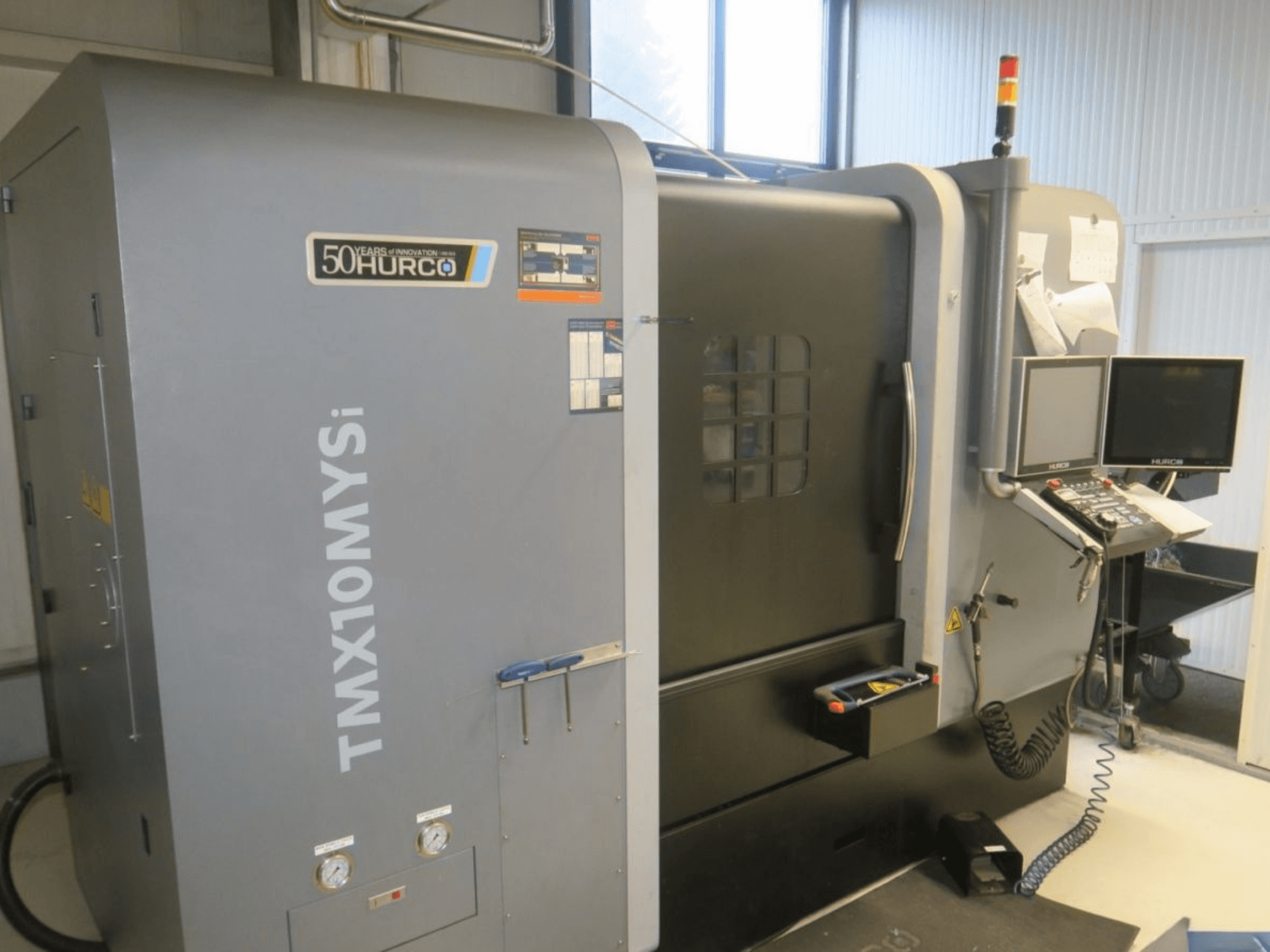 Hurco TMX10MYSi CNC-kone sivukuvassa; ohjauspaneeli, hätävalot ja näytettävät mittarit.