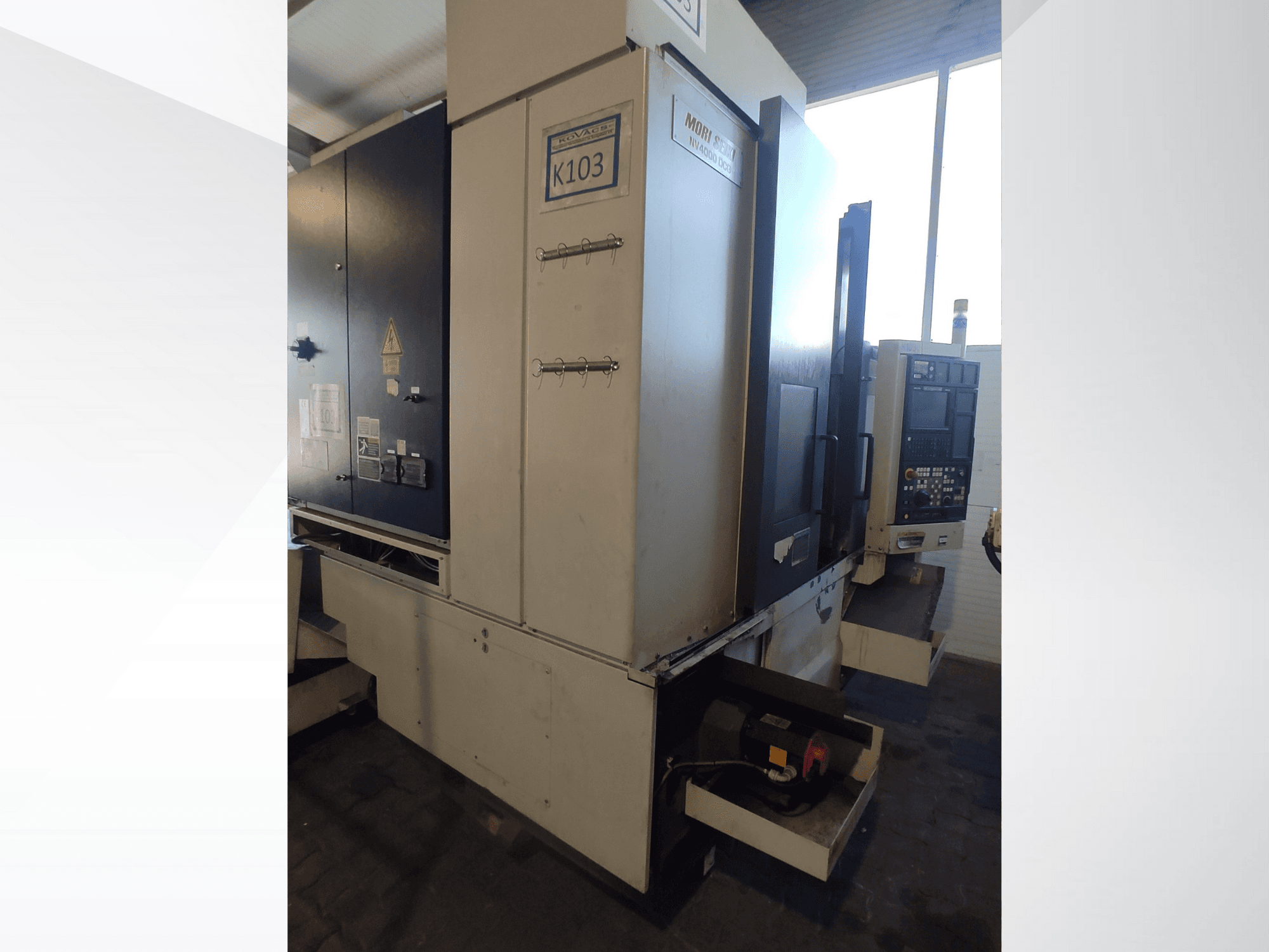Mori Seiki K103 CNC-kone etukuvassa, jossa ohjauspaneeli, turvatarrat ja sähköosat näkyvissä.