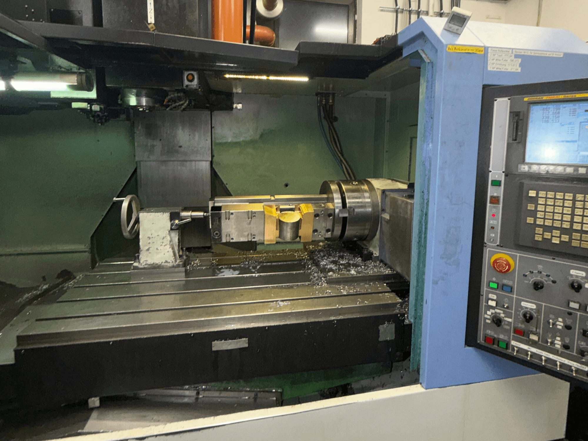 DOOSAN DNM650 -pystykoneistuskeskus, etunäkymä, jossa näkyvät leikkuutyökalu ja ohjauspaneeli sekä työpöydällä olevat metallilastut.