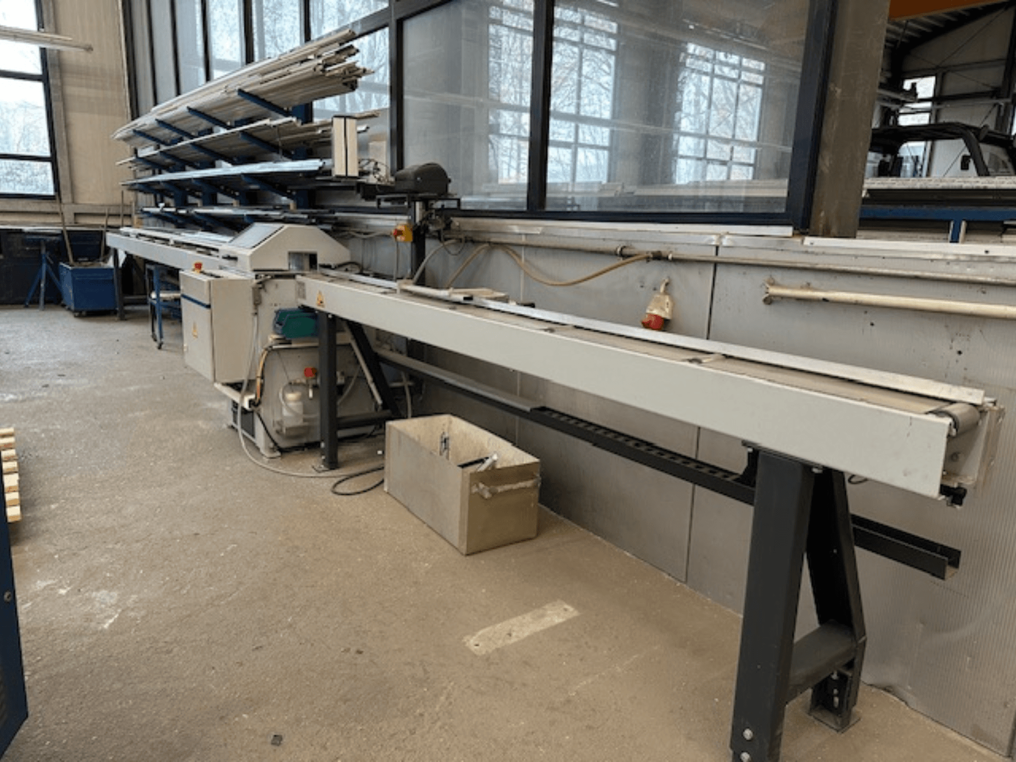 SCHÜCO PGS-metallipyörösaha työpajassa, sivukuva, jossa on säädettävä leikkuualusta ja yläpuolella metalliprofiilihylly.