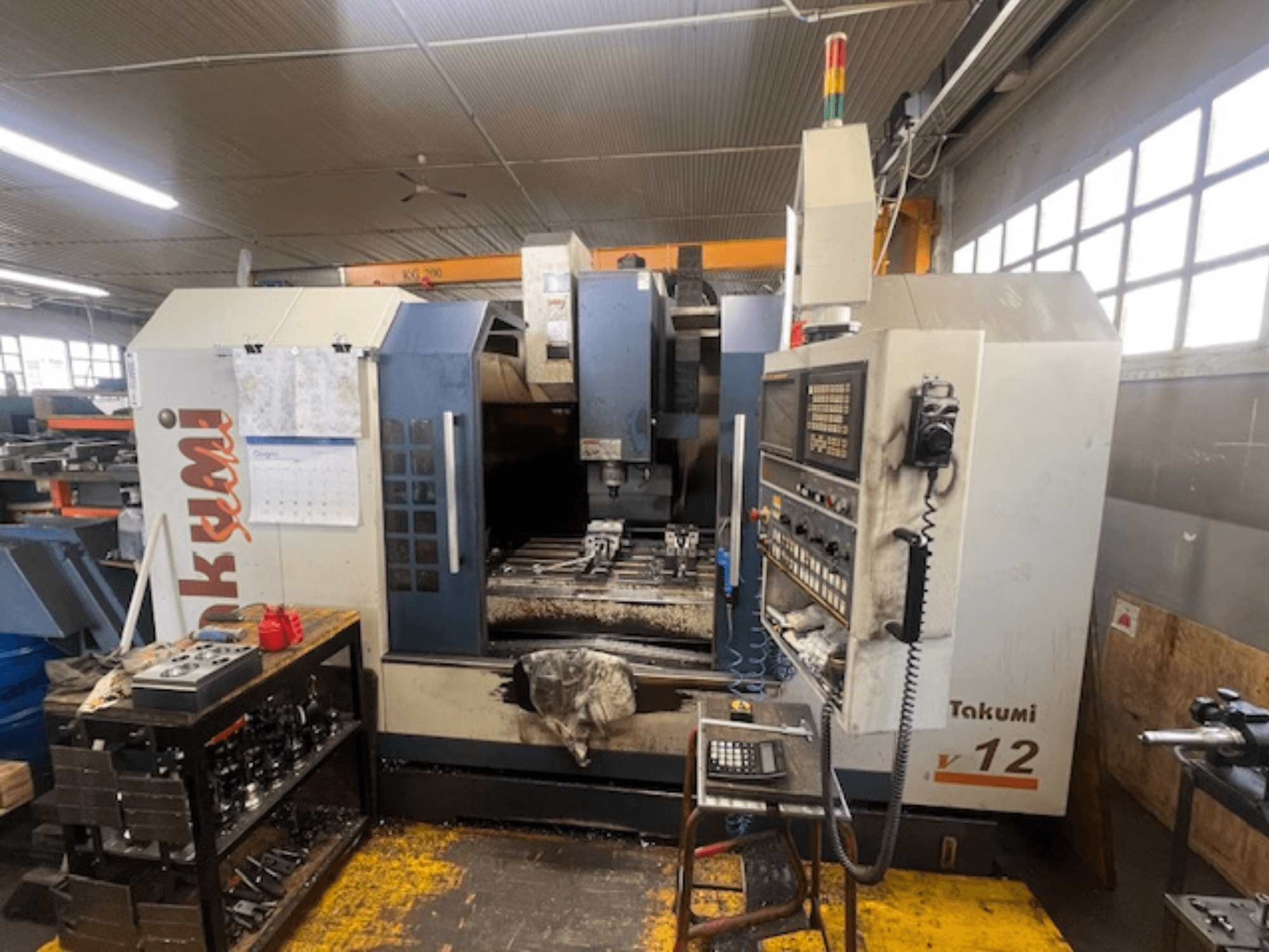 Takumi V12 CNC-jyrsinkone sivukuvassa, jossa näkyy ohjauspaneeli, leikkausalue ja työkalut työpöydällä.