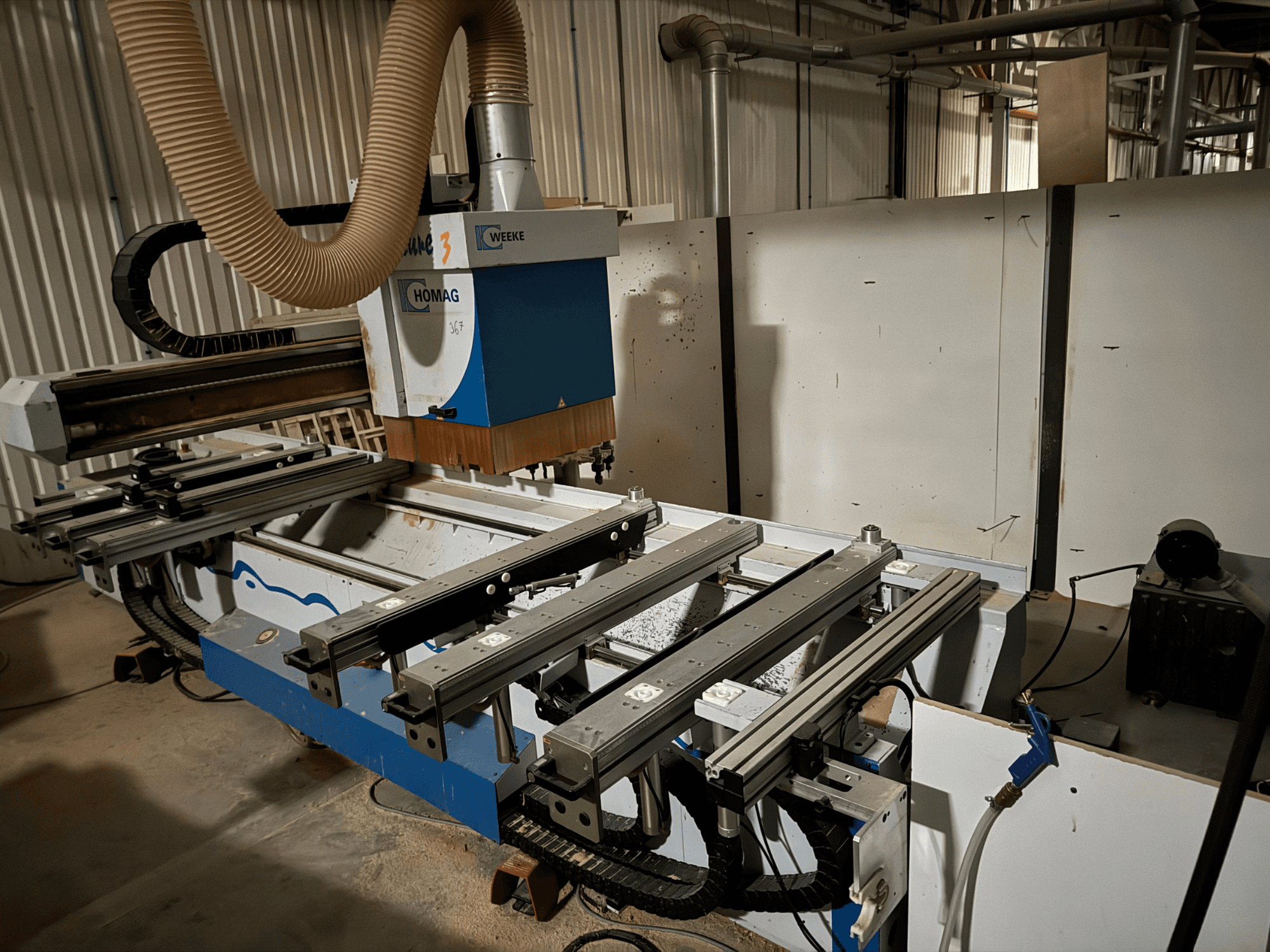 HOMAGin CNC-kone, jossa on sinivalkoinen muotoilu, sivukuva, liukukiskot, pölynpoistojärjestelmä ja asennetut työkalut.