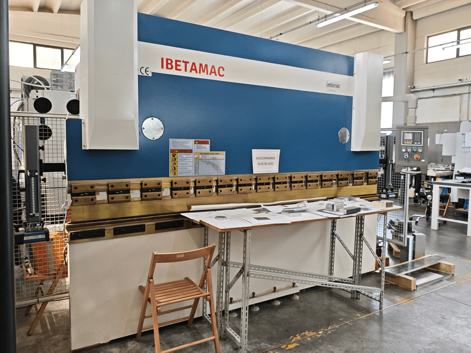 IBETAMAC 3200 100T -taivutuspenkki työpajassa, sivukuva, jossa näkyvät ohjauspaneeli, työalue ja turvallisuusohjeet.