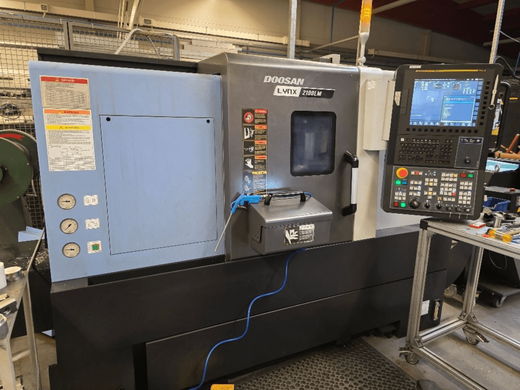 Doosan Lynx 2100LM CNC-sorvi, etukuva, jossa on ohjauspaneeli, painemittarit ja turvallisuusvaroitukset.