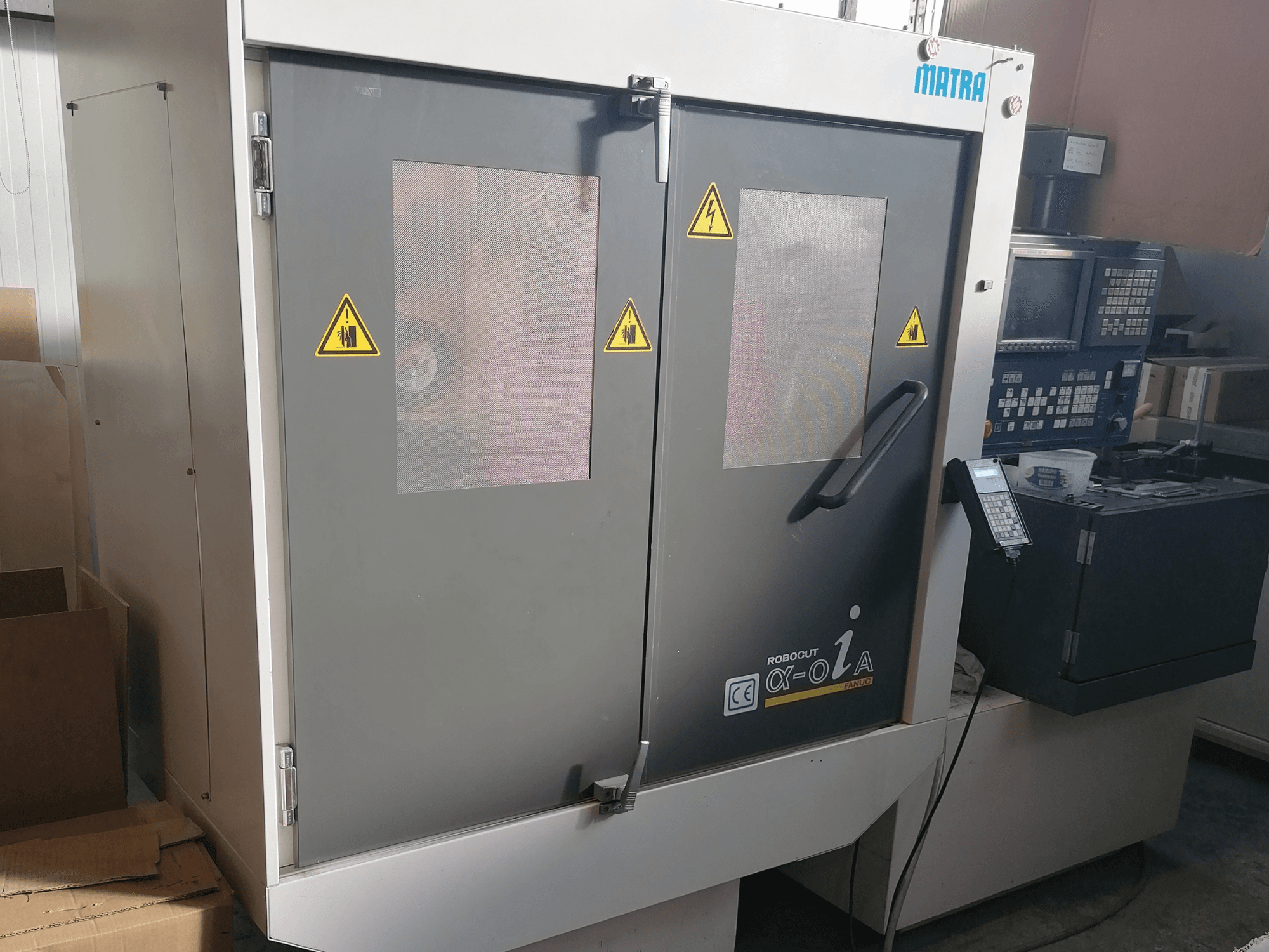 Matran Robocut α-oZα -kone, etukuva, jossa näkyvät turvavaroitukset, ohjauspaneeli ja kaksi ovea, joissa on verkkoikkunat.