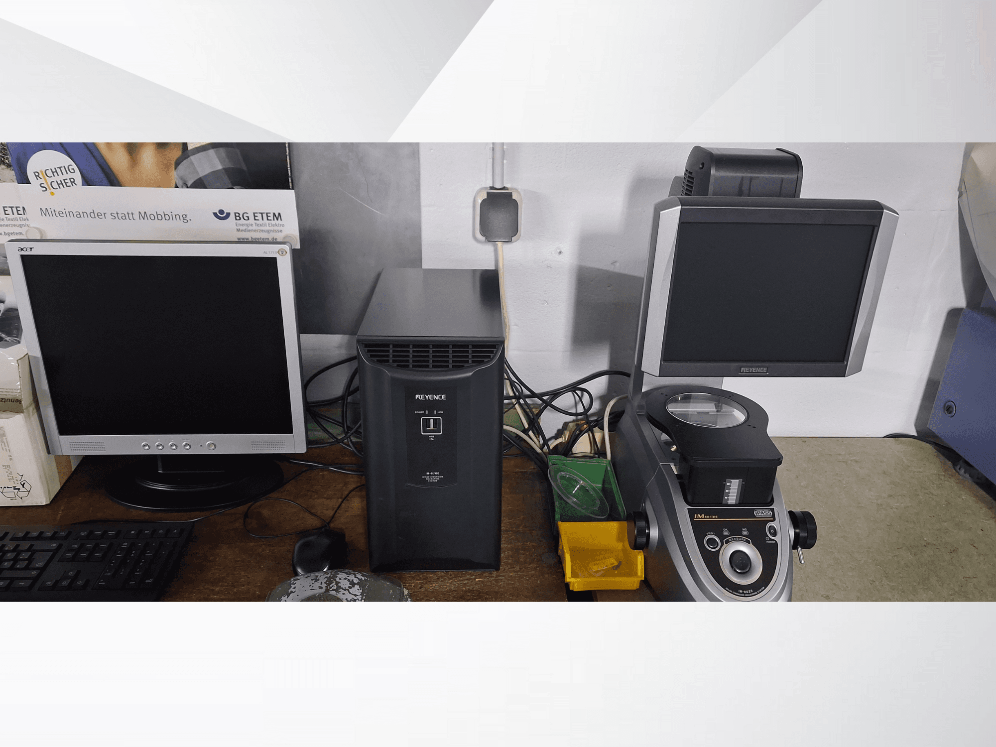 Kaksi tietokonenäyttöä, toinen Acer ja toinen Keyence, mustan laitteen ja mikroskoopin vieressä edestä katsottuna.