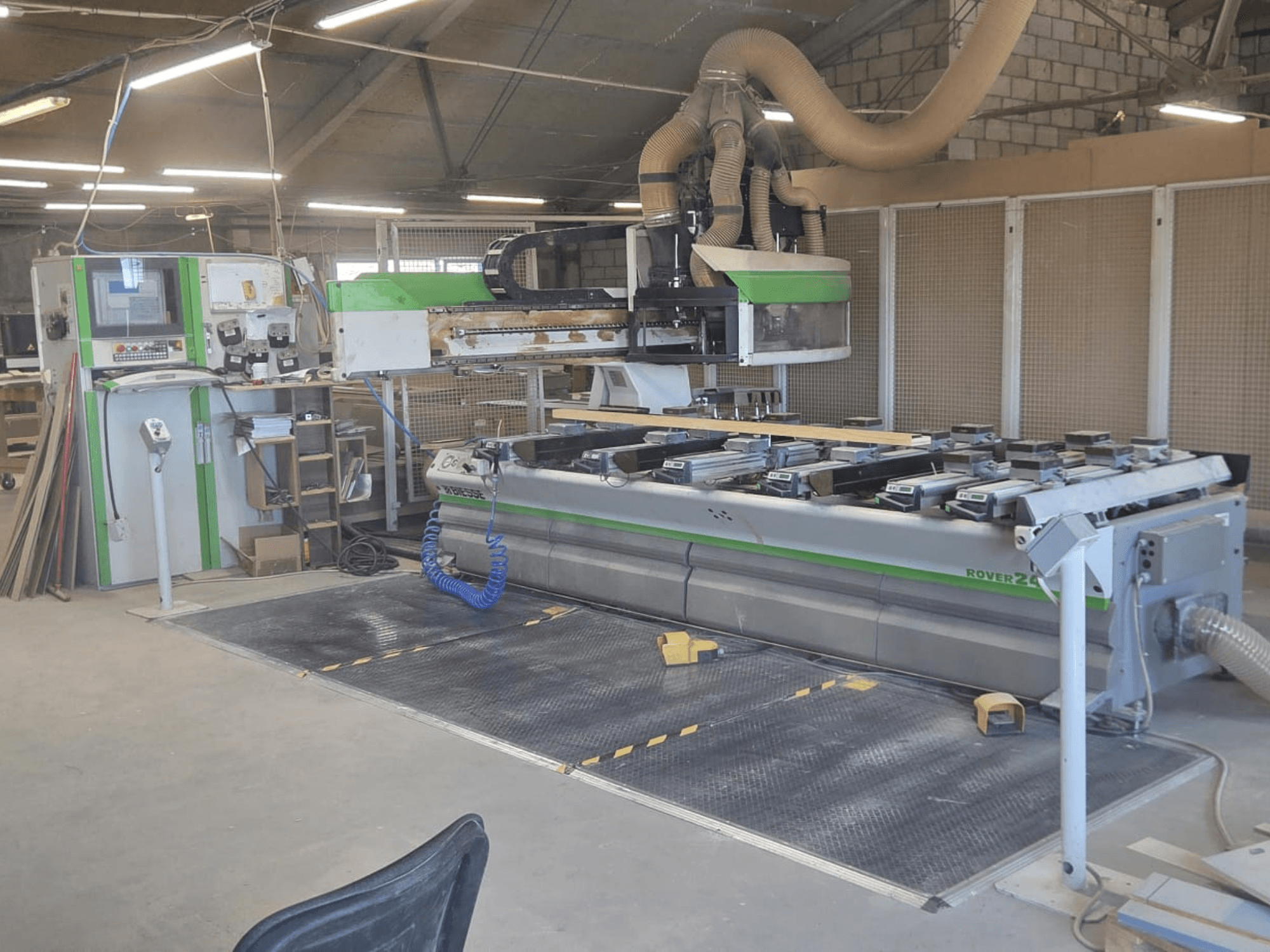 CNC-käsittelykeskus BIESSE Rover 24S työpajassa, jossa on ohjauspaneeli ja suuri työtaso puukappaleilla.