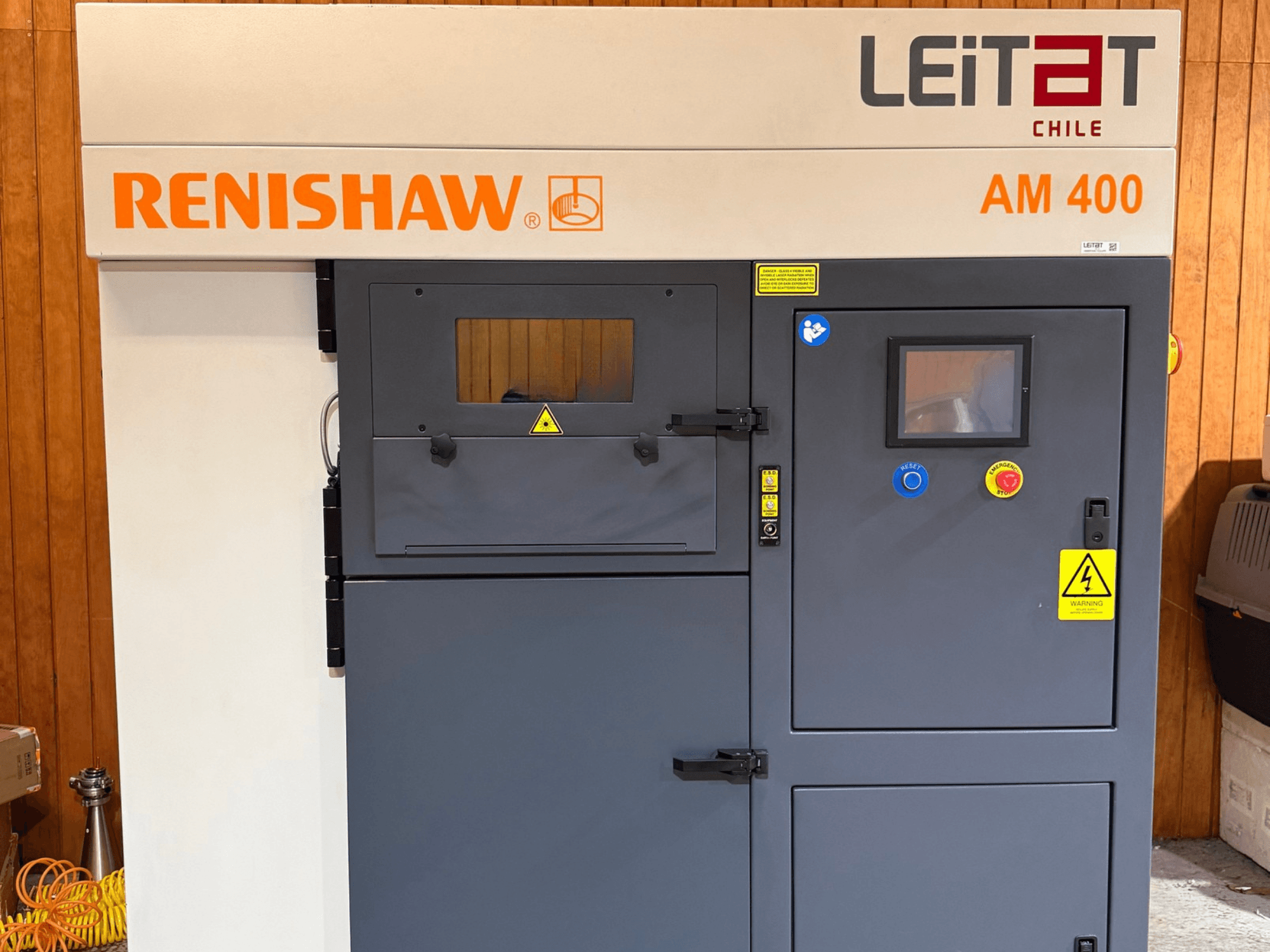 RENISHAW AM400 -metallinen 3D-tulostimen etunäkymä, jossa näkyvät ohjauspaneeli, varoitusmerkinnät ja huoltotilan luukku.