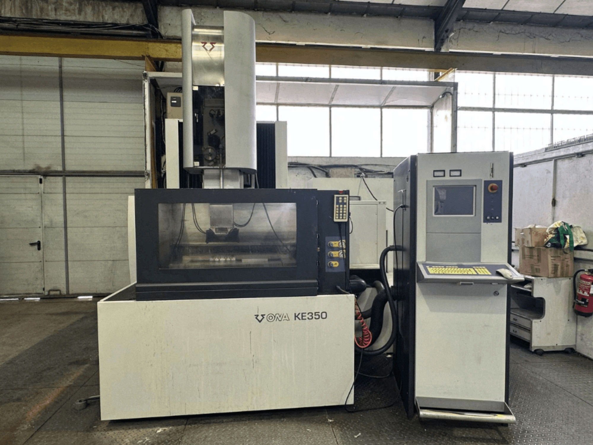 Etunäkymä ONA KE350 CNC-koneesta, jossa on ohjauspaneeli, näyttö ja erilaisia painikkeita teollisuusympäristössä.