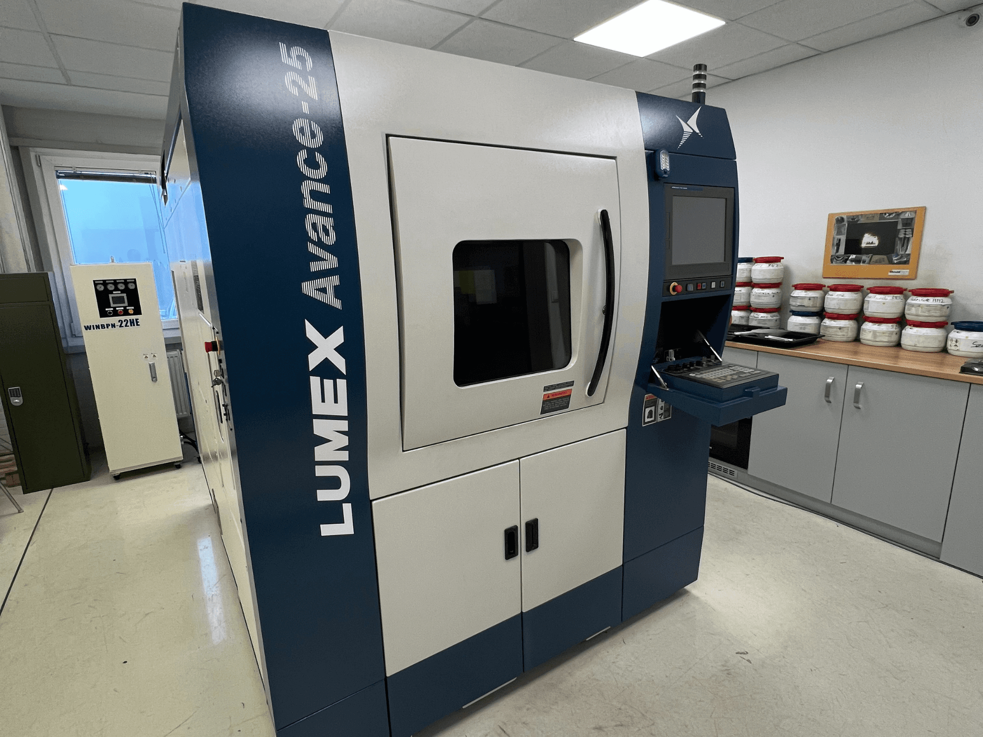 LUMEX Avance-25 3D-tulostin laboratorioympäristössä, etukuva. Ohjauspaneeli, jossa näyttö ja painikkeet näkyvissä, laitteet taustalla.