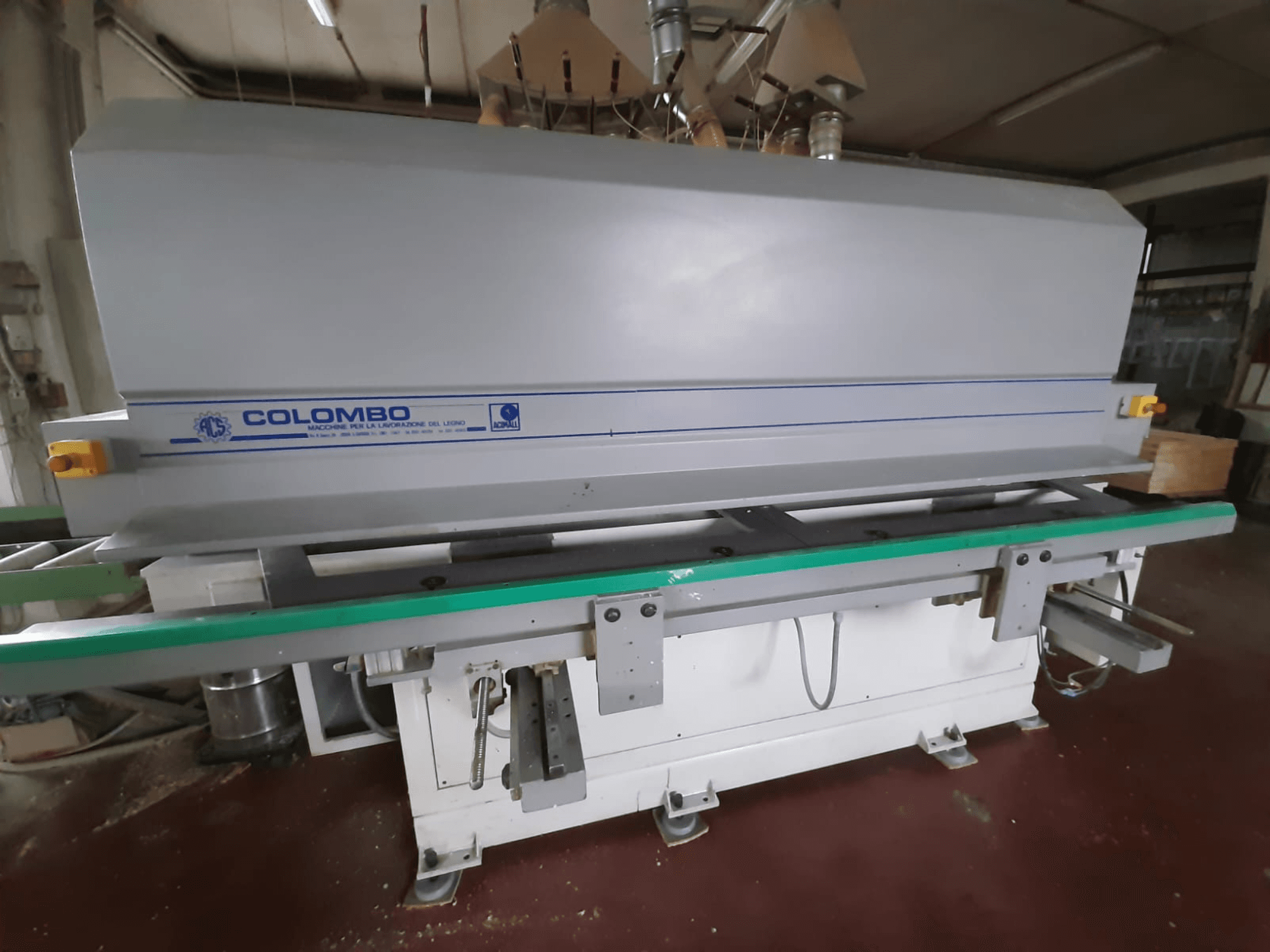Colombon puunjalostuskone, etukuva, jossa on pitkä vihreä pöytä, ohjauspainikkeet ja harmaa runko, jossa on sinisiä korostuksia.