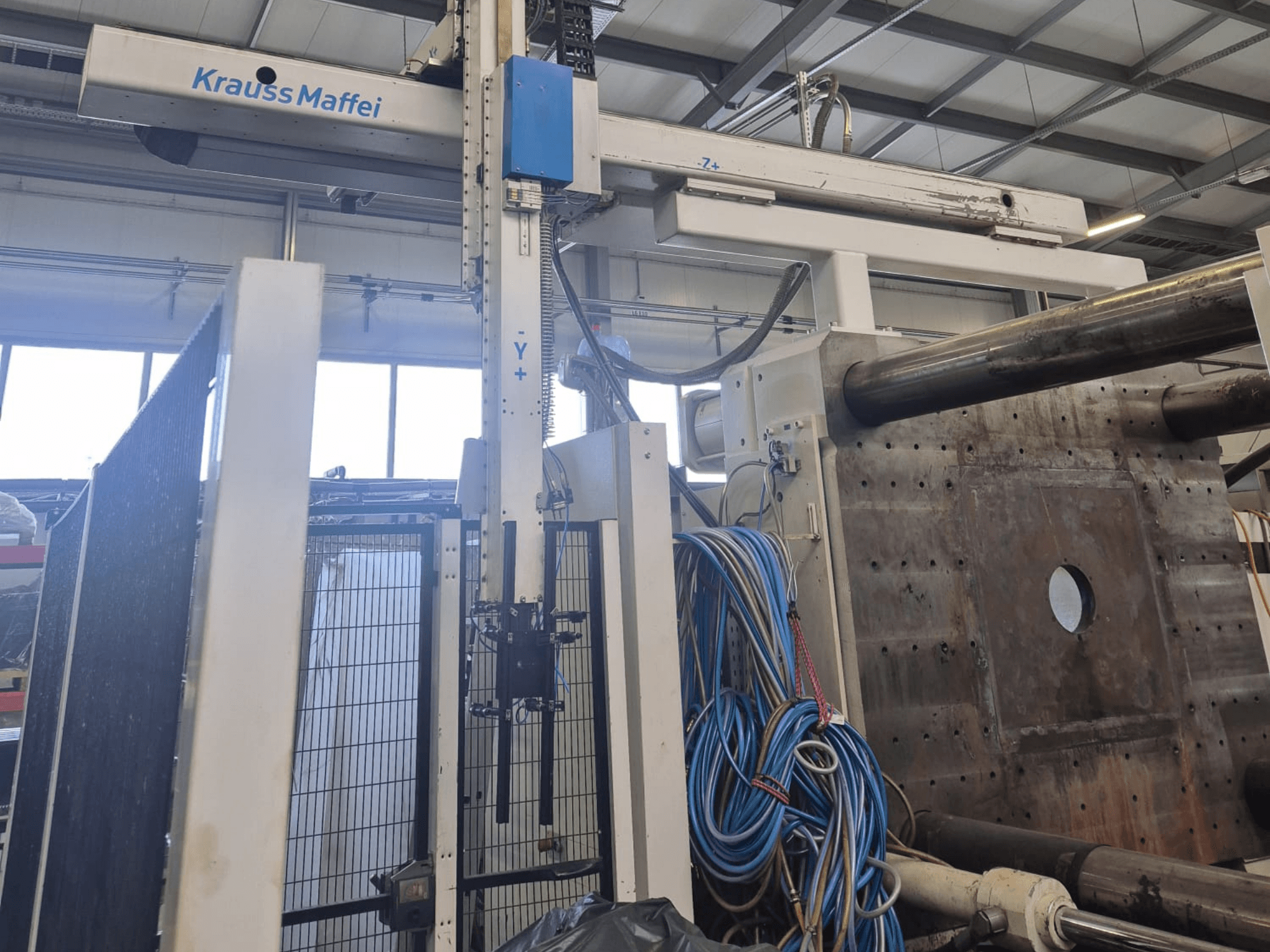 Krauss Maffei 1300-12000 MX -hydraulinen ruiskuvalukone, etunäkymä mekaanisine varsineen ja hydrauliikkaliitoksineen.