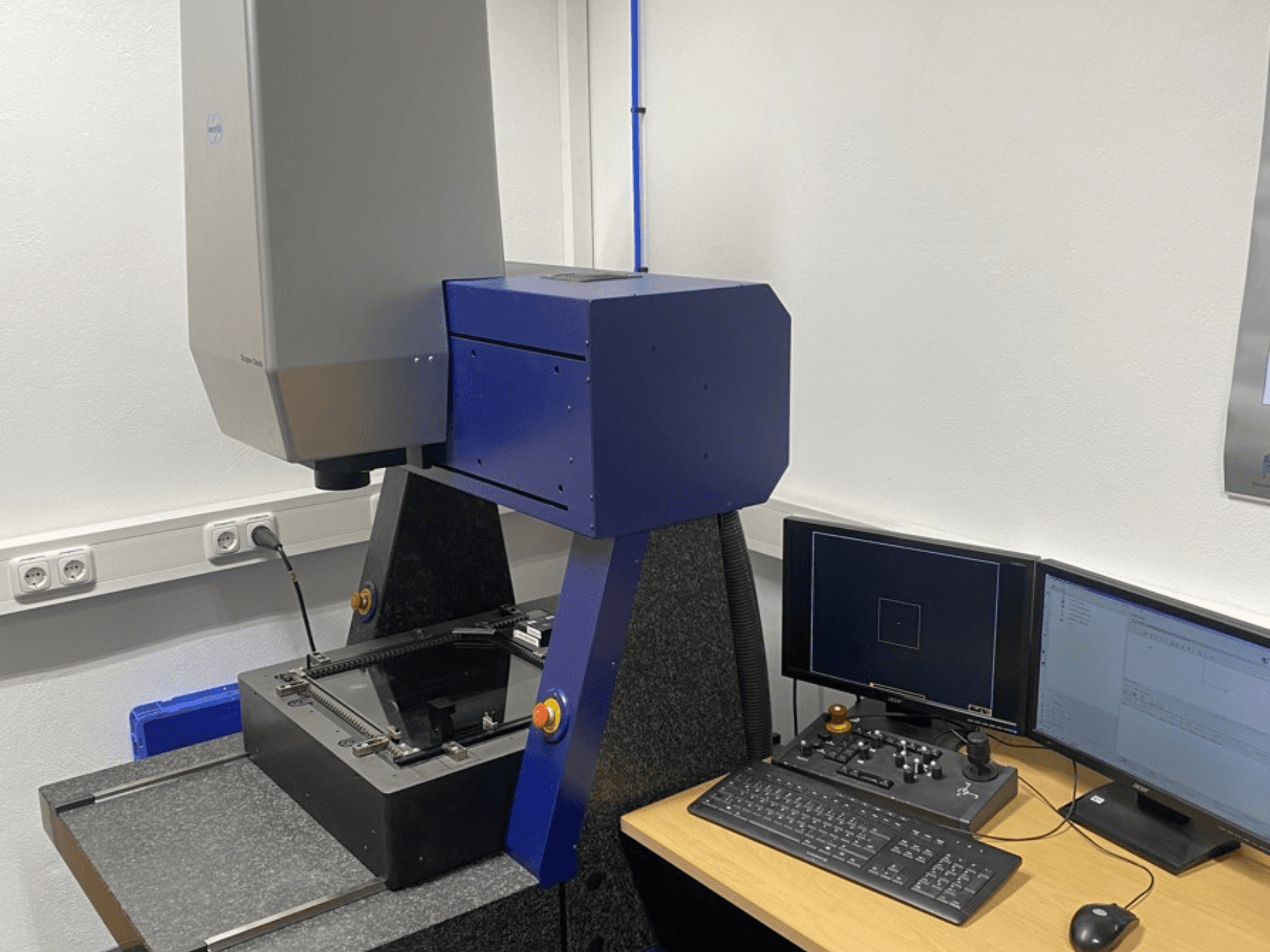 Werth Scope-Check 400 CMM -mittalaite laboratoriossa, jossa näkyy mittapää ja ohjauspaneeli näytöillä ja näppäimistöllä.