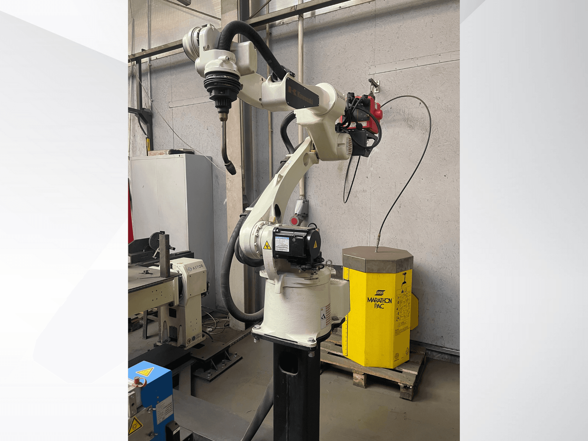 Kawasakin robottikäsivarsi sivukuvasta, jossa on asennettu työkalunpidin, taustalla keltainen voimayksikkö.