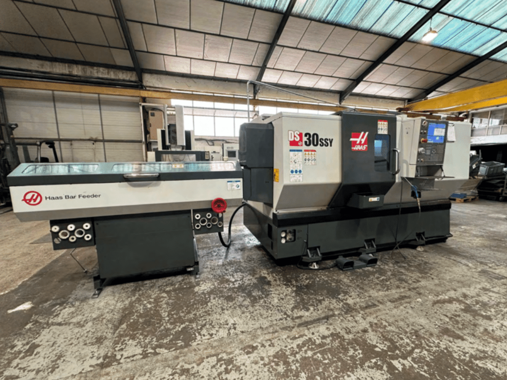 Haas DS-30SSY CNC-sorvi Haasin tankosyöttölaitteella, sivukuva ohjauspaneelista ja syöttölaitteesta työpajassa.