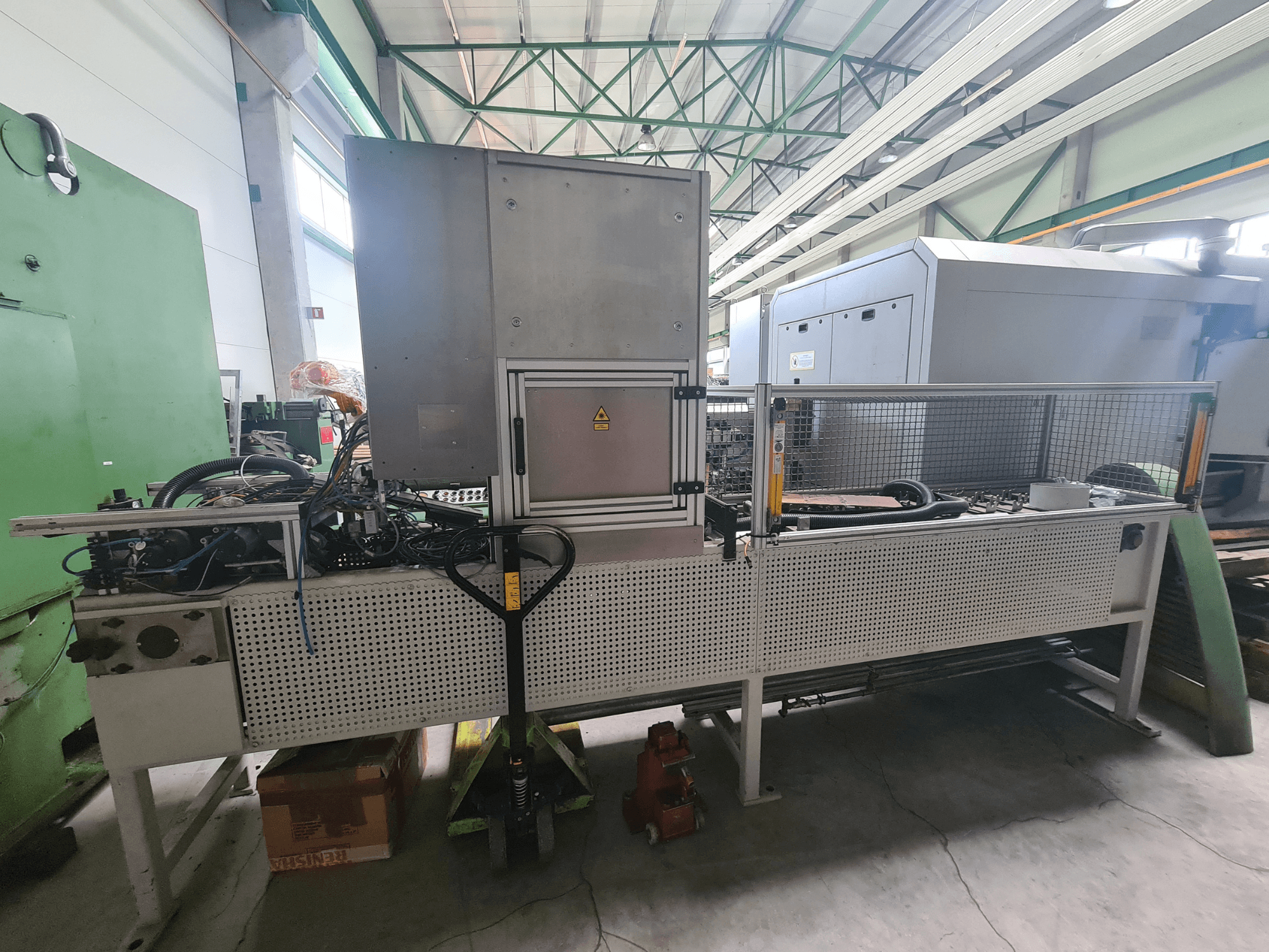 Teollisuuskone, jossa on metallirunko, letkuja ja ohjauspaneeli, sivulta katsottuna tehdasympäristössä.