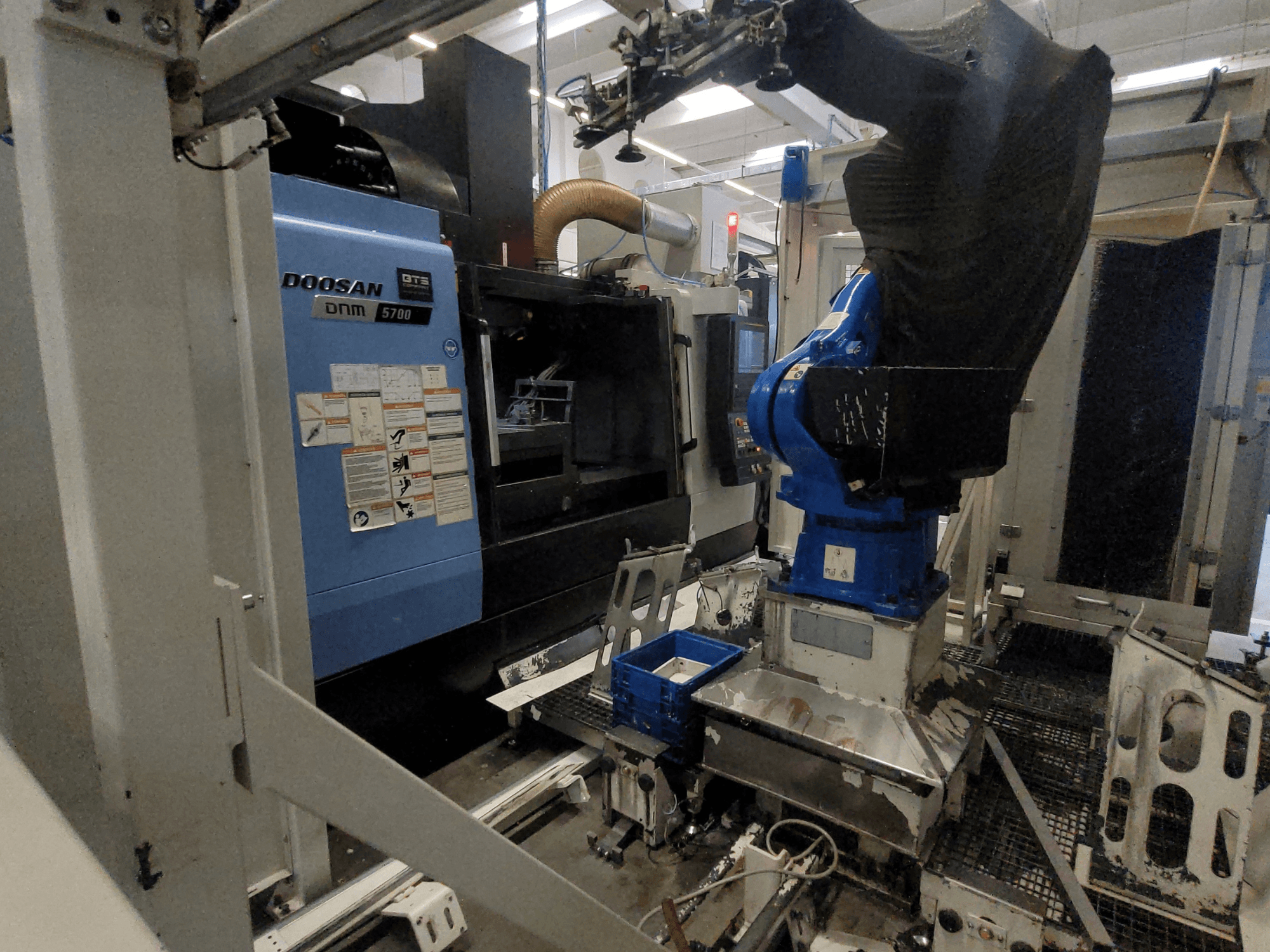 DOOSAN DNM 5700 -pystykoneistuskeskus tehdasympäristössä; kuvassa näkyy laitteen etunäkymä ja robottikäsivarren integrointi.