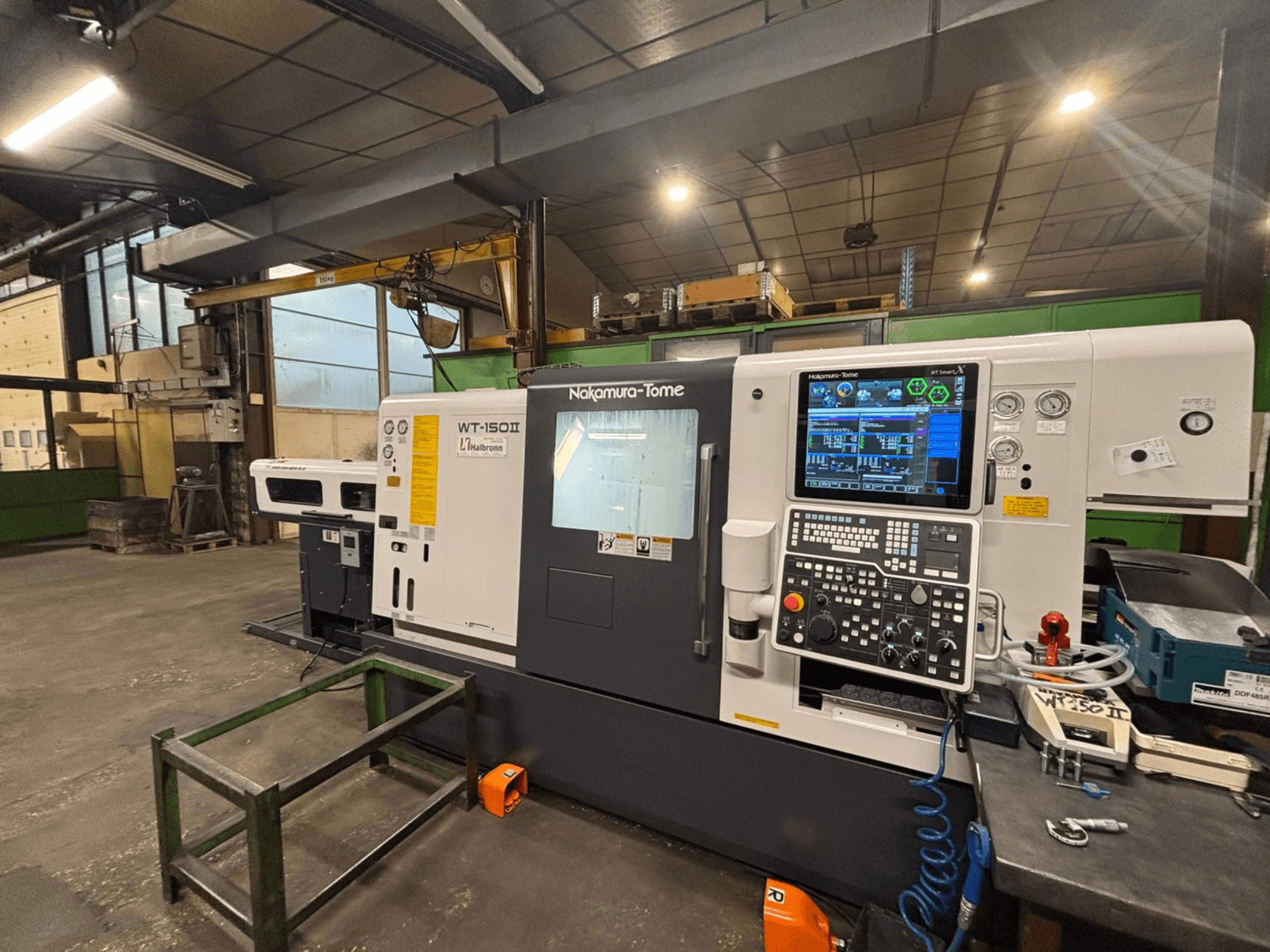 Nakamura-Tome WT-150II -kone, etukuva, jossa ohjauspaneeli ja työkalut ovat näkyvissä työpöydällä työpajassa.