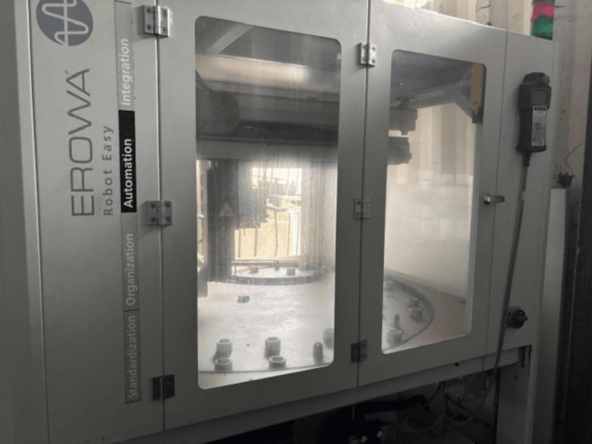 EROWA Robot Easy Automationin etunäkymä; siinä on läpinäkyvät ovet, näkyvät automaatiokomponentit ja ohjauspaneeli.