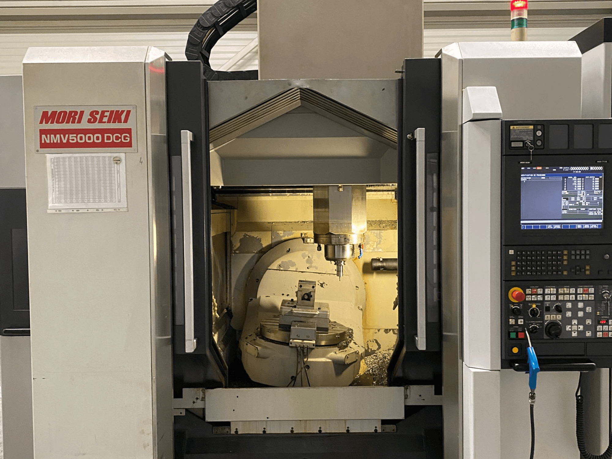 MORI SEIKI NMV 5000DCG yleiskoneistuskeskus, etukuva, jossa näkyy ohjauspaneeli ja sisäpuolinen koneistusalue.