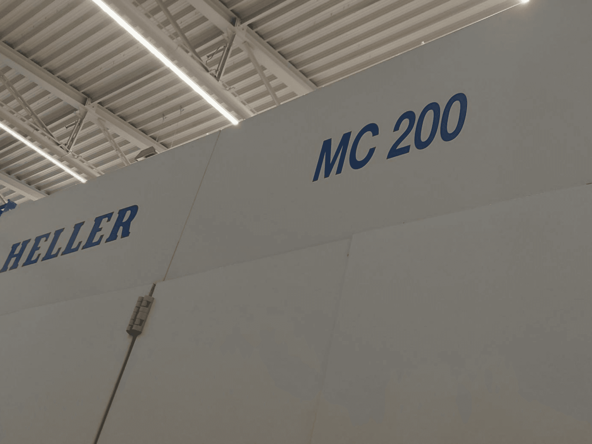 Heller MC 200 -vaakakoneistuskeskus sivulta kuvattuna, merkin ja mallin korostus sinisin kirjaimin valkoisella pinnalla.