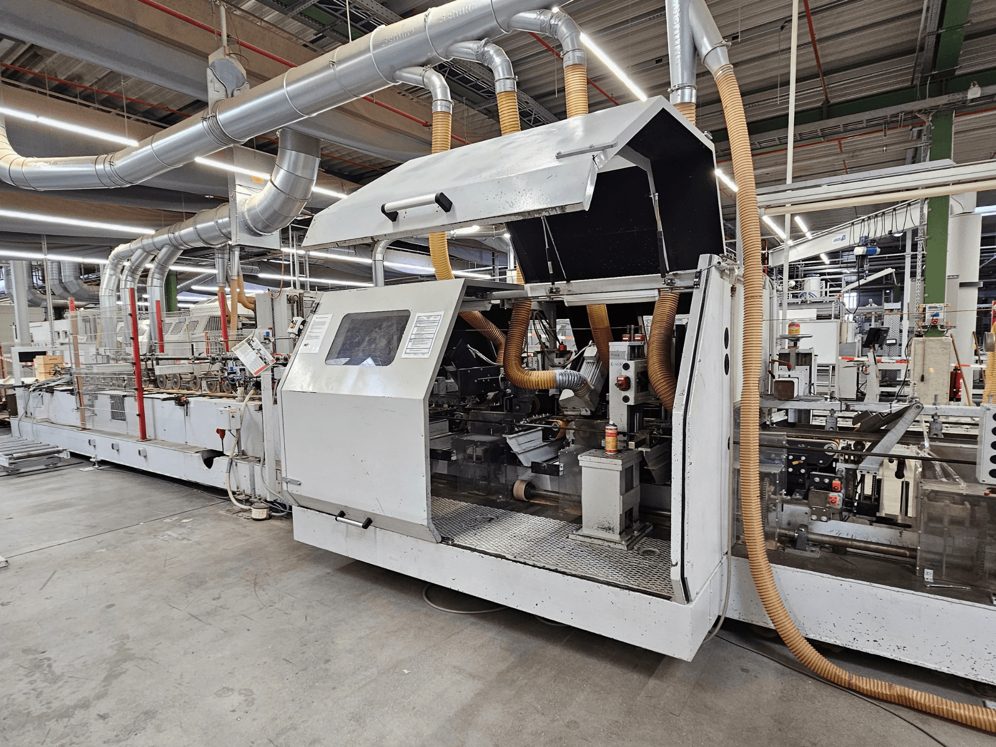 HOMAG FG63 -särmäyslaite tehtaalla, sivukuva, jossa näkyvät käyttöosat ja pölynpoistojärjestelmä.