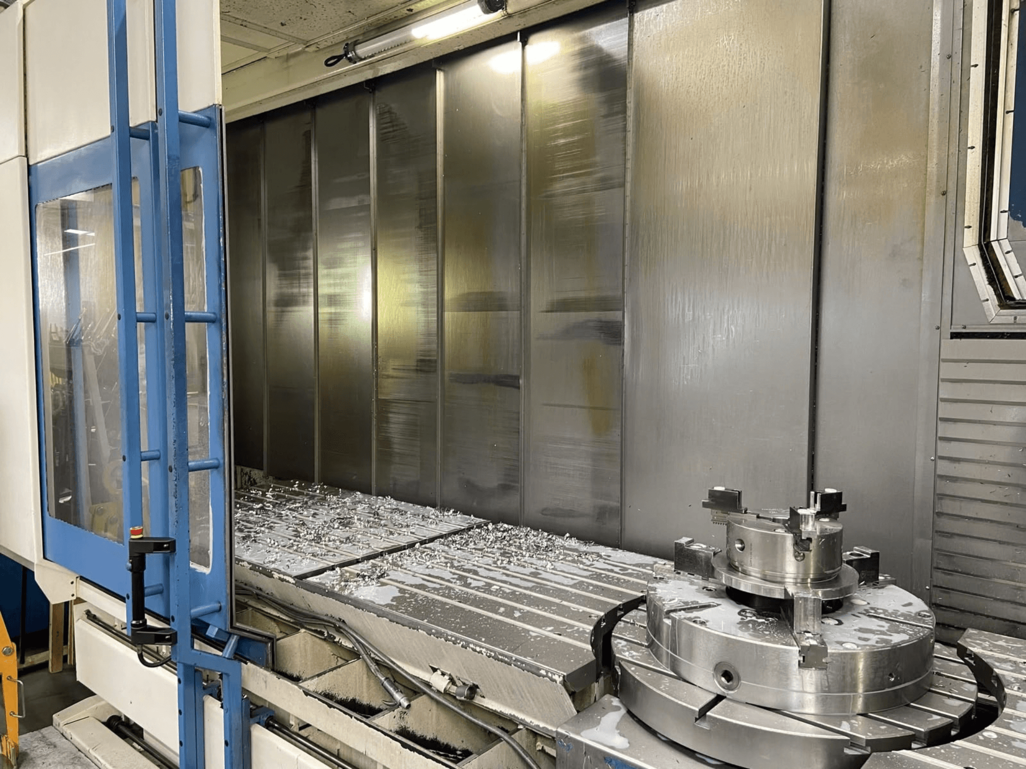 AXA VHC-3-3000-M/E -pystykoneistuskeskus, etunäkymä, jossa näkyy työpöydällä olevia jyrsittyjä metallilastuja ja leikkuutyökaluja.