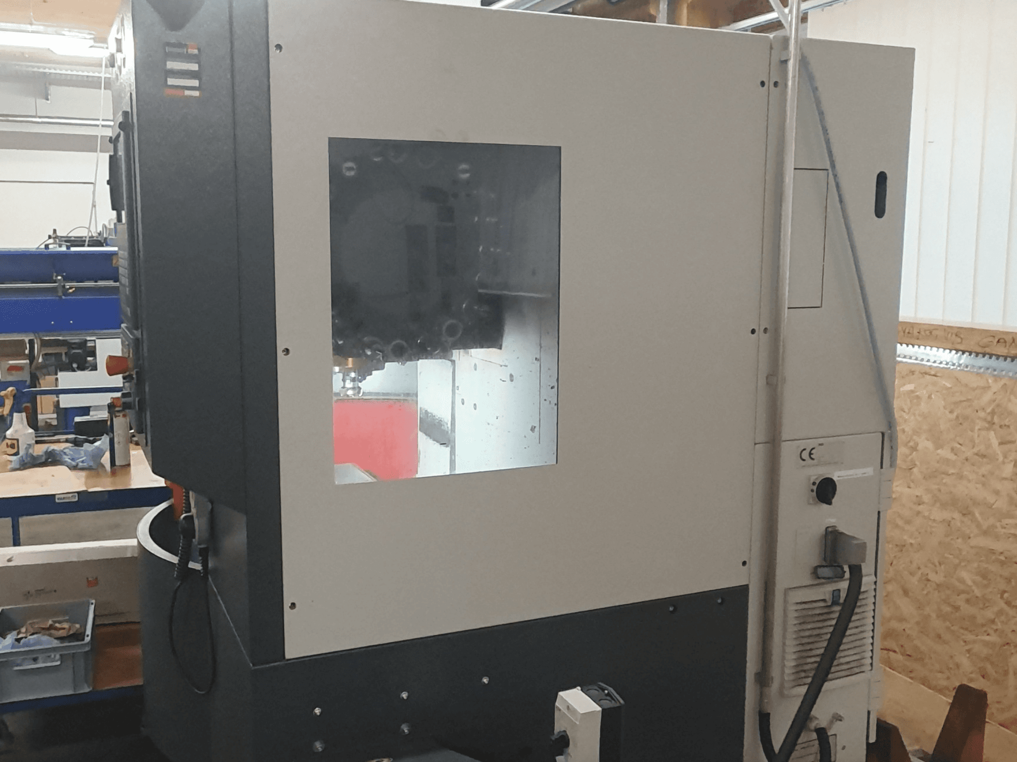 Sivukuva metallintyöstökoneesta, jossa on näkyvä ohjauspaneeli, suuri katseluikkuna ja monimutkaisia sisäosia.