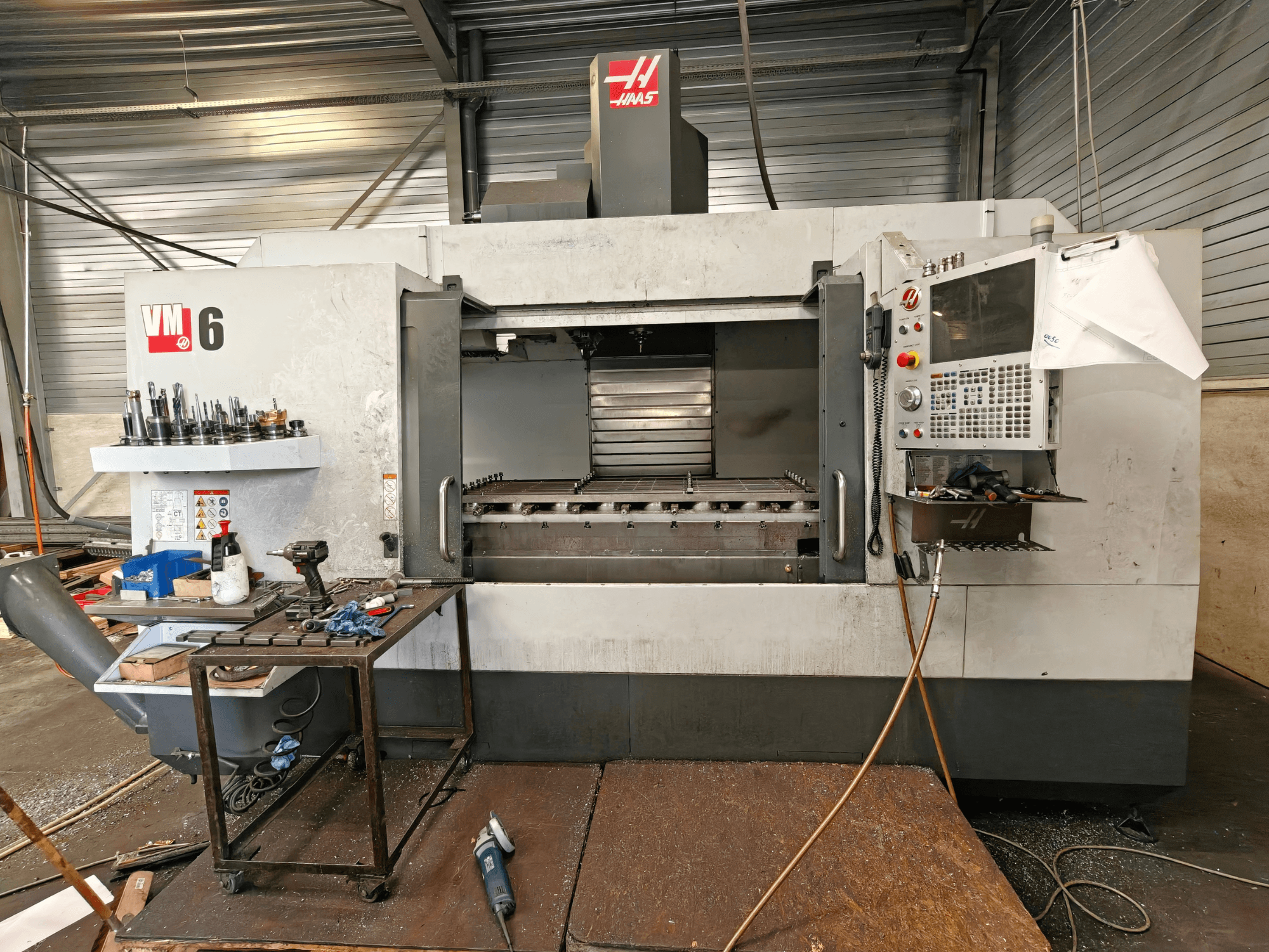 Haas VM-6 -pystykoneistuskeskus, etunäkymä, jossa näkyvät työkaluvarasto, ohjauspaneeli ja työtilan roskat.