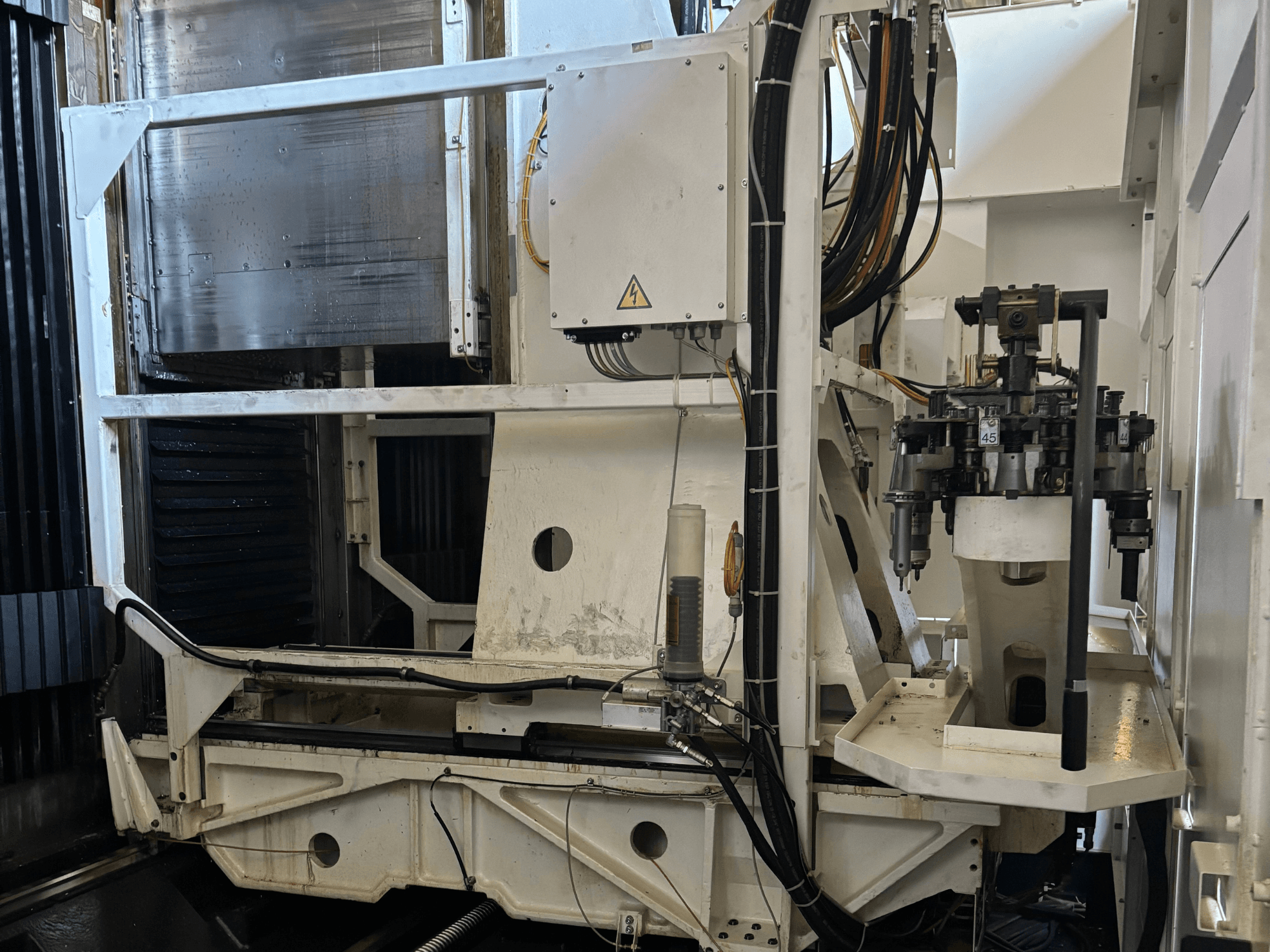 Teollisuuskoneen sivukuva valkoisesta CNC-jyrsinkoneesta, jossa on näkyvissä työkaluja, putkia ja ohjauspaneeli.