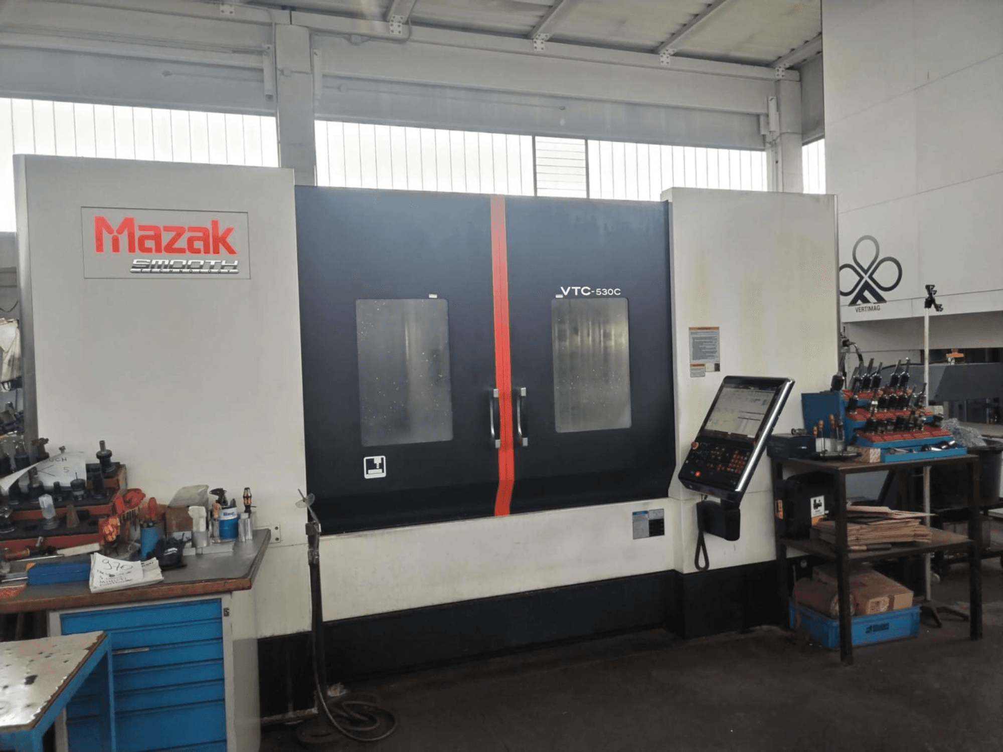 Mazak VTC-530C -pystykoneistuskeskus työpajassa; kuvassa näkyy ohjauspaneeli ja sivupöydällä olevat työkalut.