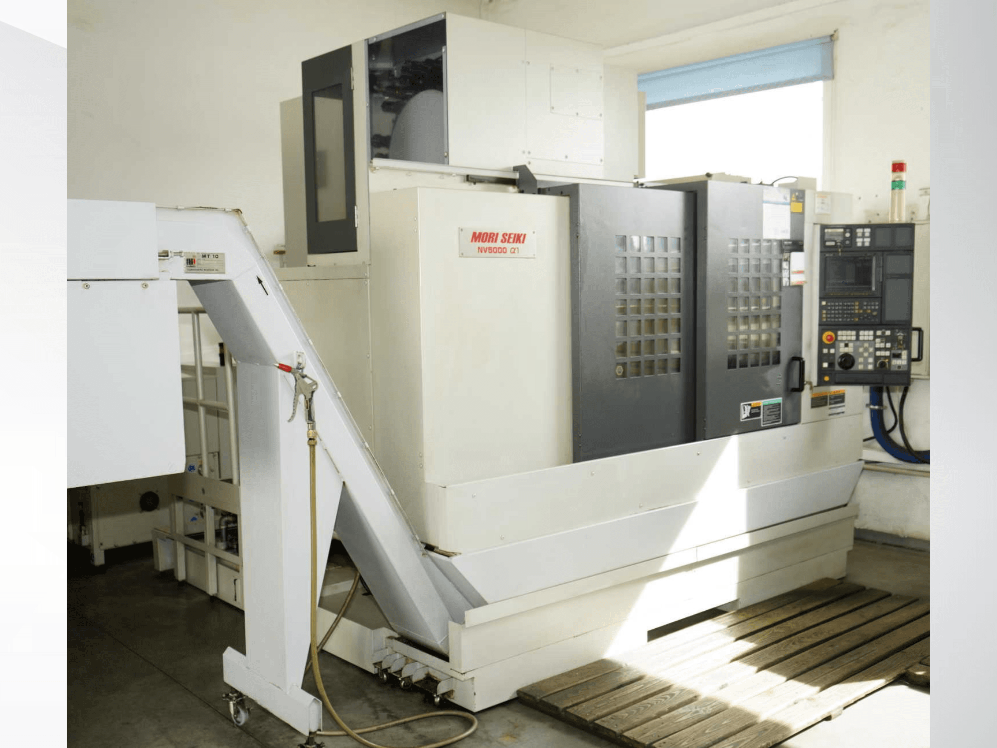 MORI SEIKI NV 5000 alpha1 -pystykoneistuskeskus edestä katsottuna; kuvassa näkyvät ohjauspaneeli, turvaominaisuudet ja lastausalue.