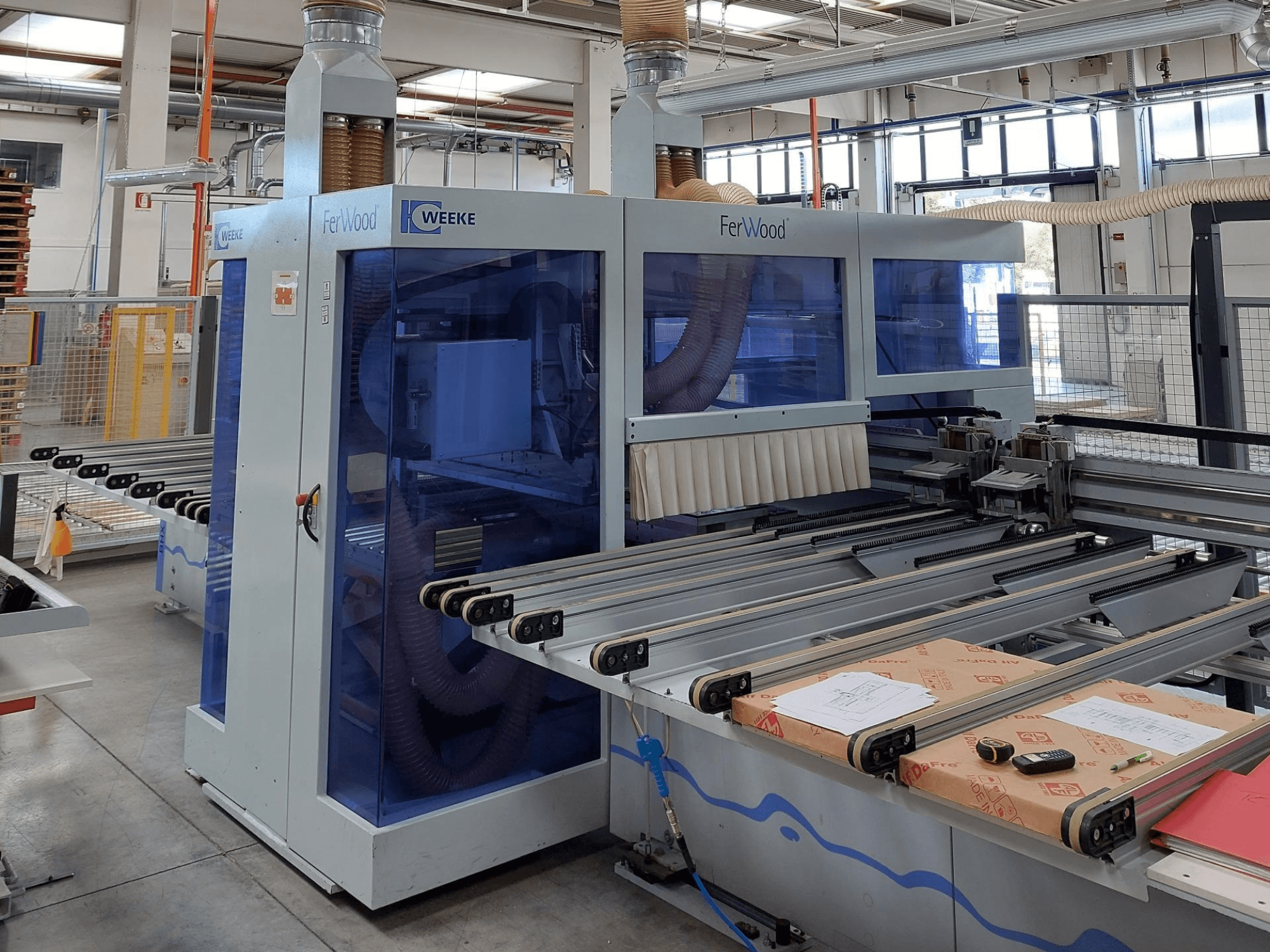 Weeke FerWood CNC-kone työpajassa, etukuva, jossa näkyy sinisävyiset paneelit, ohjauspainikkeet ja työpöytä materiaaleineen.
