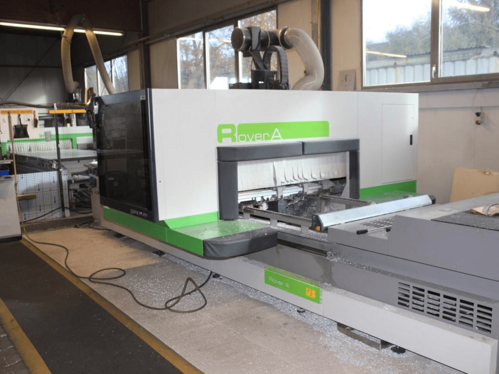 BIESSE Rover A 1232 CNC-jyrsin, sivukuva, jossa näkyy leikkausalue ja ohjauspaneeli teollisuusympäristössä.