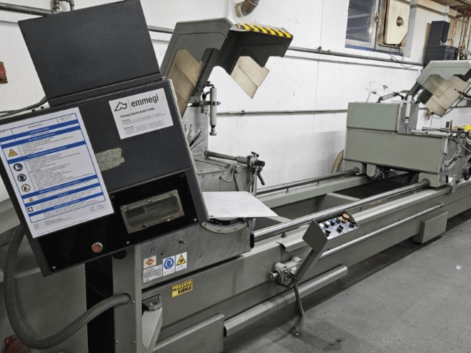 Emmegi-teollisuusleikkauskone, etukuva, jossa on ohjauspaneeli, turvatarrat ja käyttöosat.