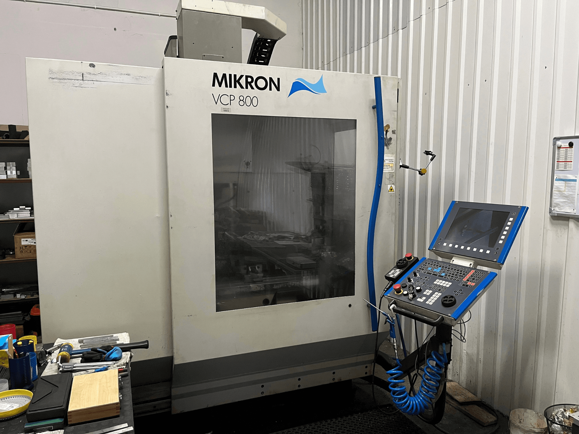 MIKRON VCP 800 -pystykoneistuskeskus, etunäkymä, etualalla työpöydällä oleva ohjauspaneeli ja työkalut.