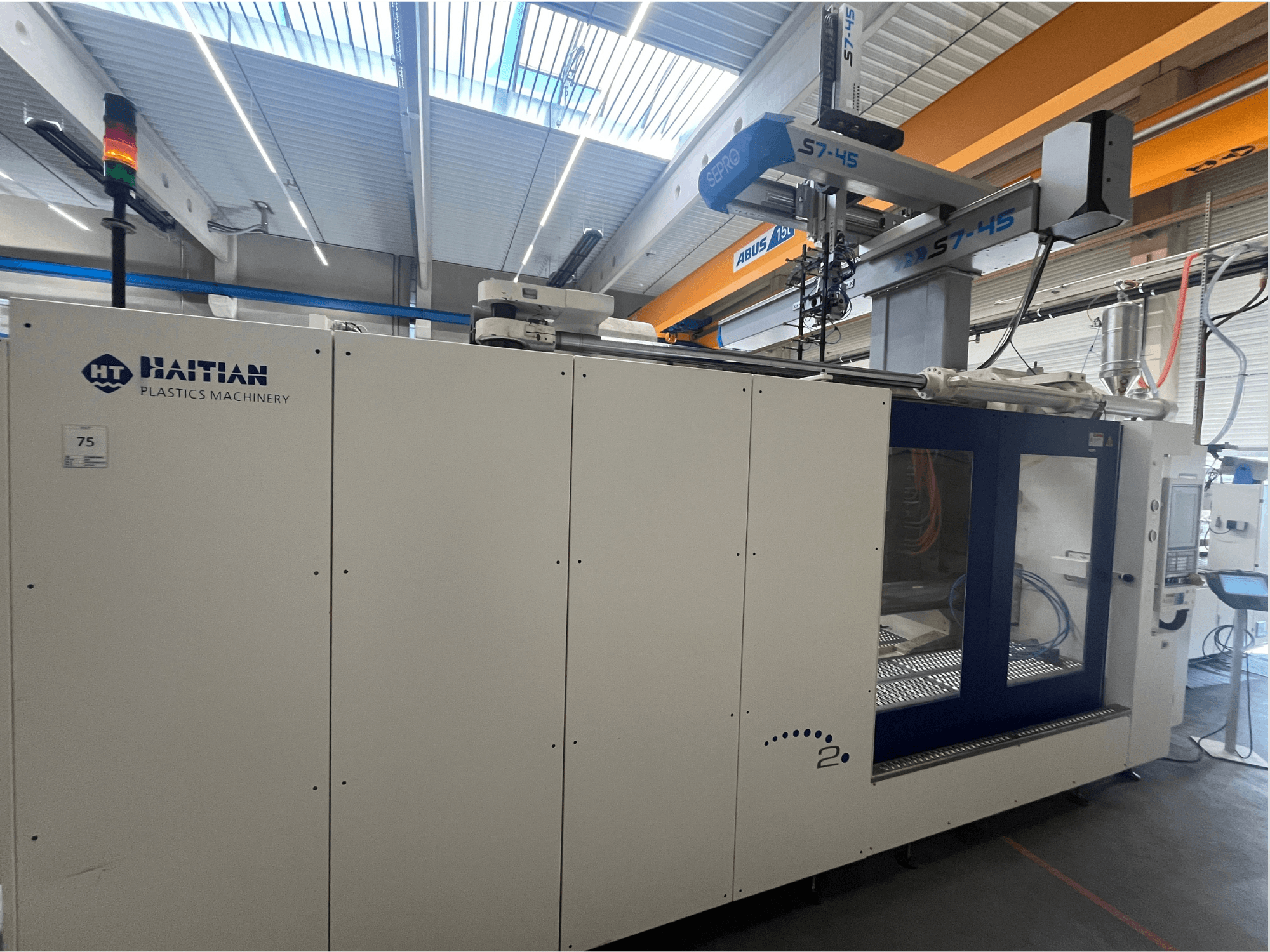 Haitin S7-45 ruiskuvalukone sivukuvassa, jossa on ohjauspaneeli ja turvavaloilmaisin. Valkoinen ja sininen muotoilu.