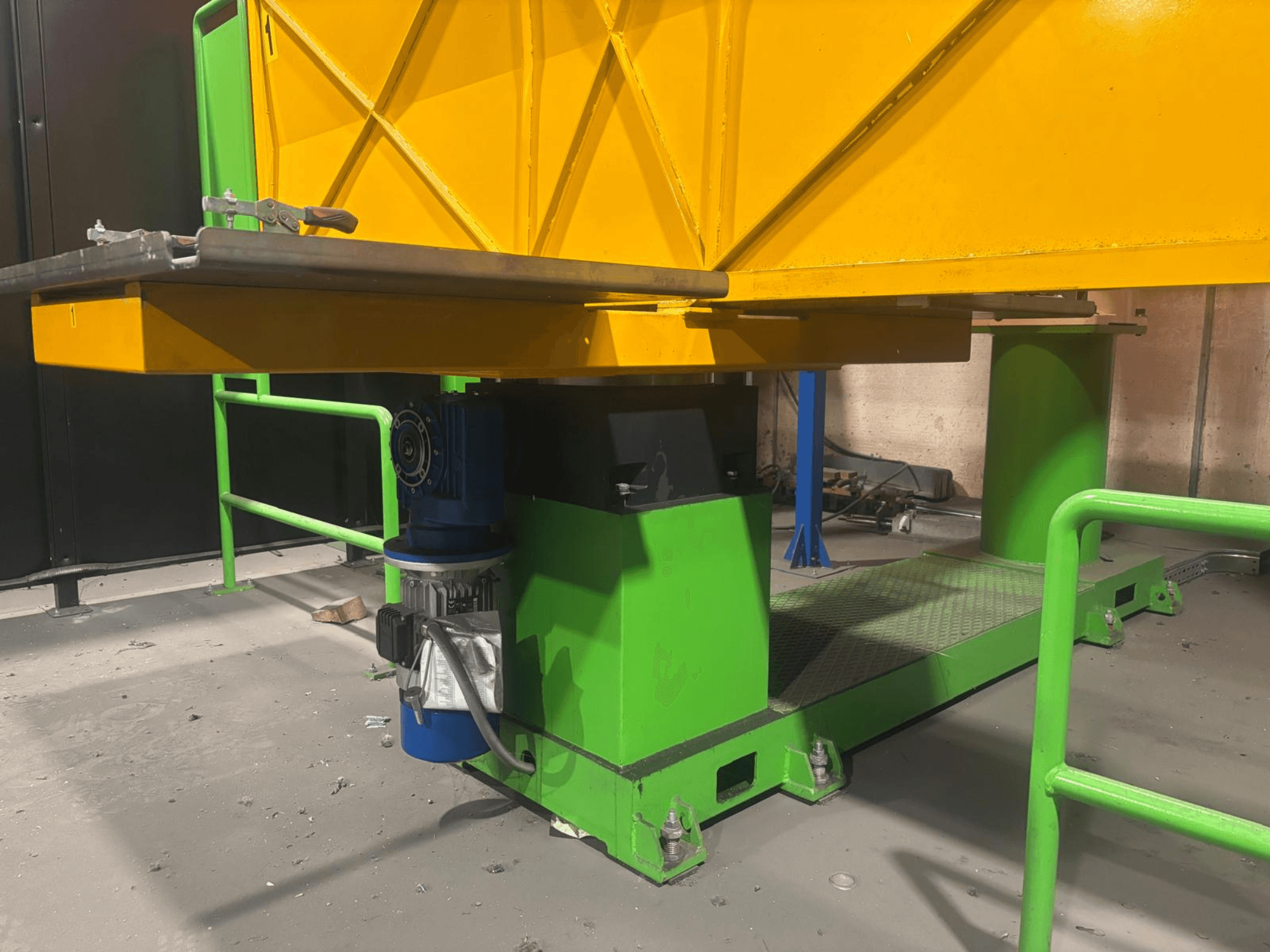 Vihreä ja keltainen teollisuuskone matalasta etukuvasta, jossa on moottori ja alusta, jossa on kuvioitu pinta.